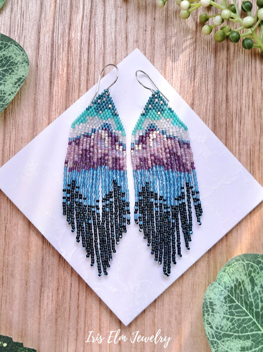 Beadwoven mountain forest lake seed bead fringe earrings surrounded by greenery with Iris Elm Jewelry branding