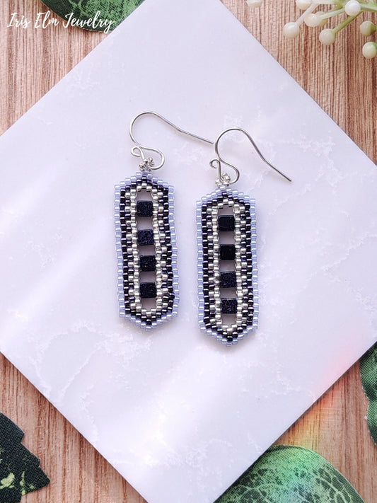 Beaded blue goldstone cube earrings on a white napkin with a wooden surface underneath