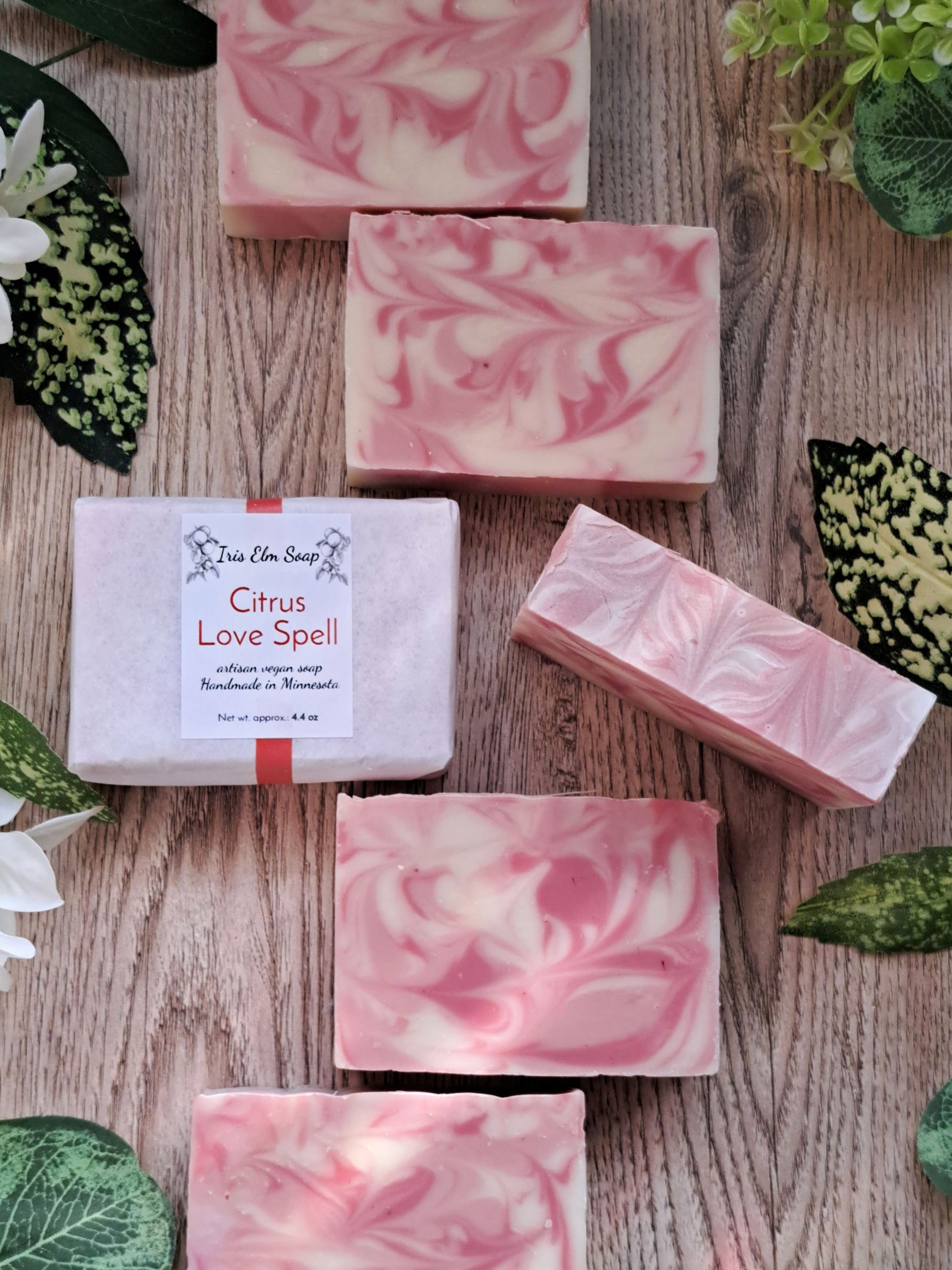 Pink and white swirled soap bars on a wooden surface with a label reading 'Citrus Love Spell'.