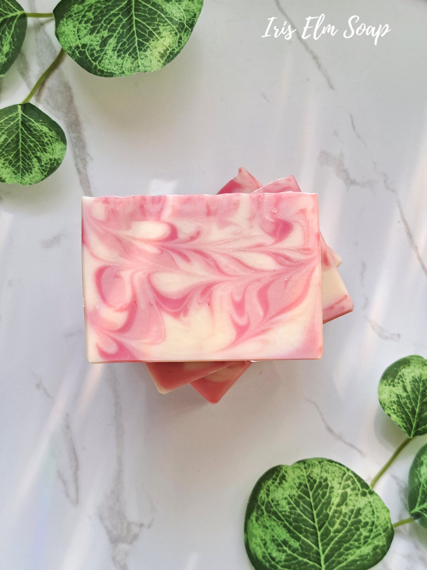 Pink and white swirled citrus love spell handmade soap bar on a marble surface with green leaves.