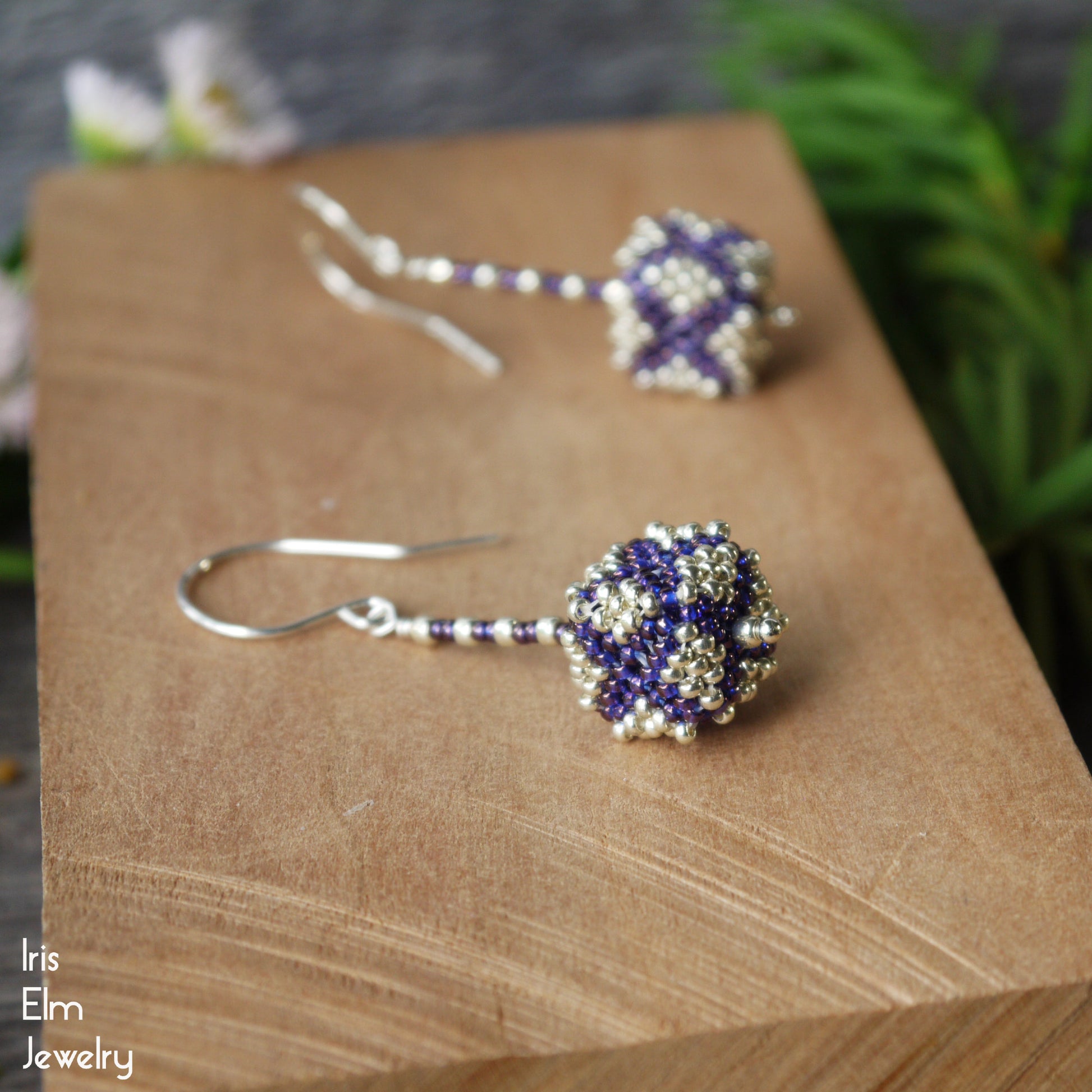 Beaded purple and silver seed bead cube shaped earrings on a wooden surface with 'Iris Elm Jewelry' branding.
