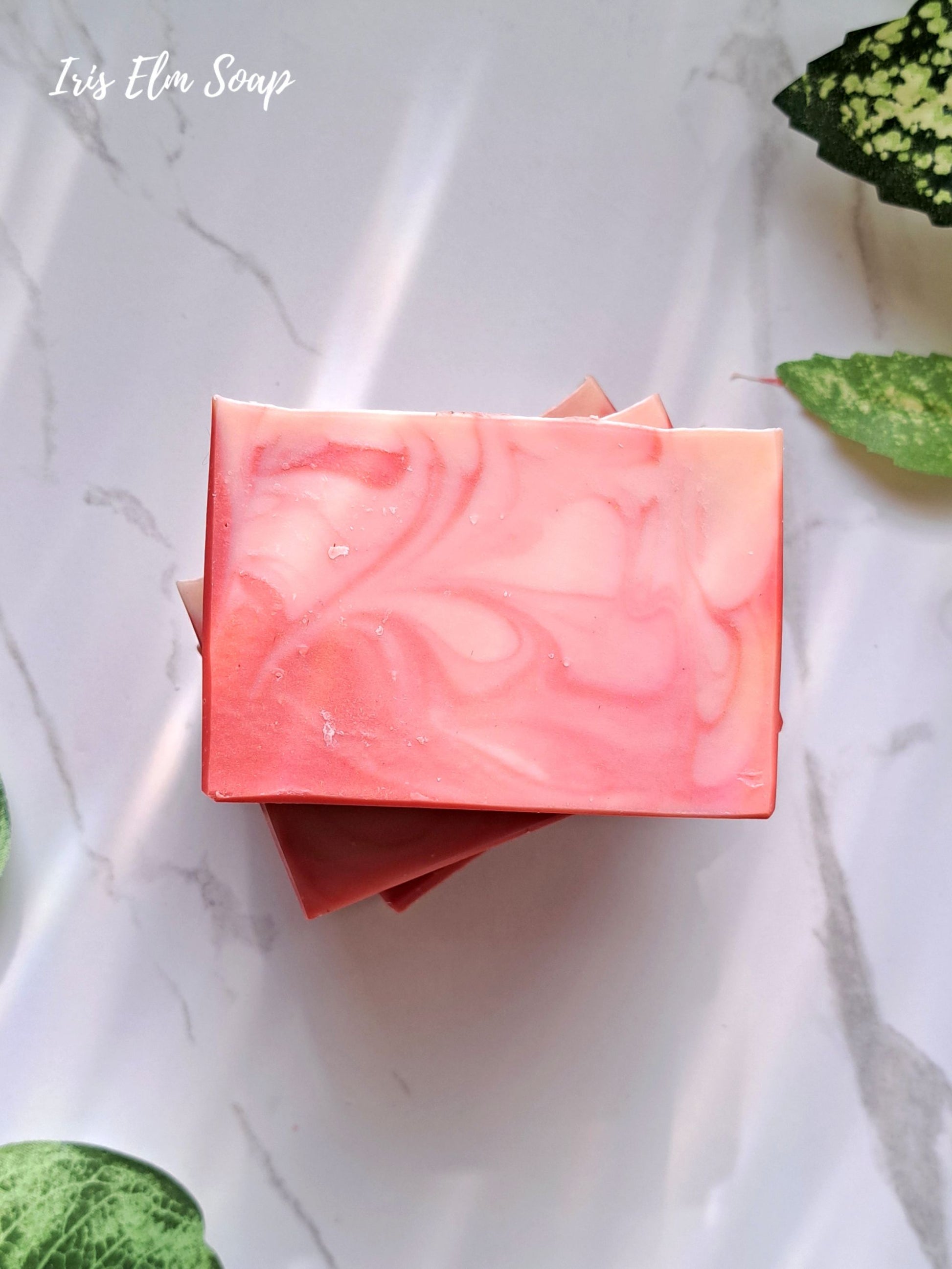 Pink peach bellini handmade soap bar with marbled pattern on a white marble surface with green leaves.
