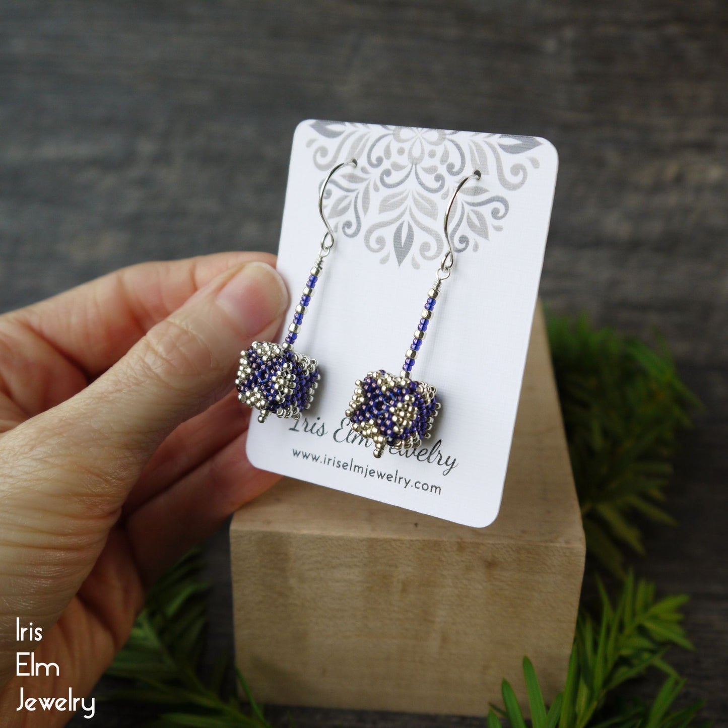 purple and silver seed bead cube shaped beadwork earrings on a card held by a hand with a natural background