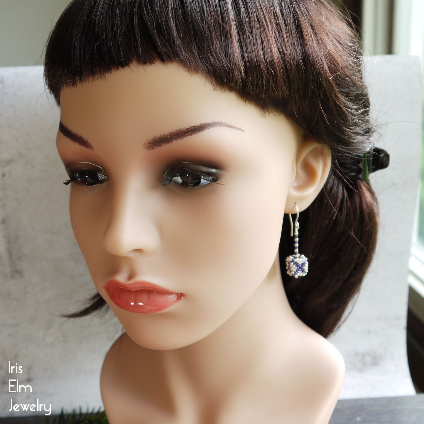 Mannequin head with dark hair and purple and silver seed bead cube shaped earrings, featuring Iris Elm Jewelry branding.