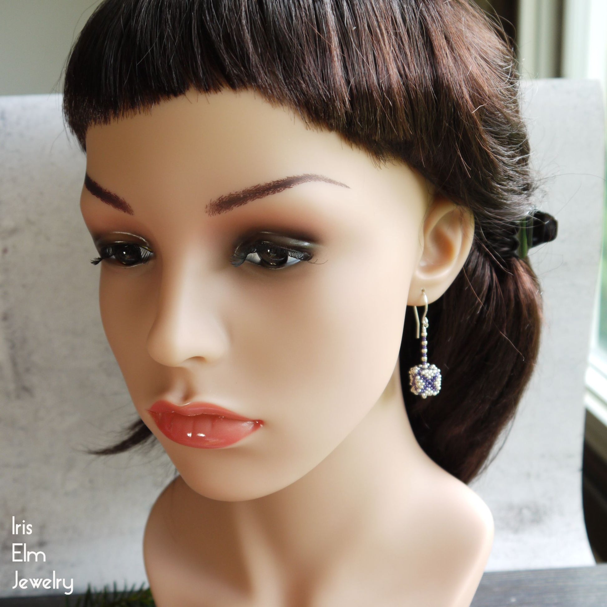 Mannequin head with dark hair and purple and silver seed bead cube shaped earrings, featuring Iris Elm Jewelry branding.