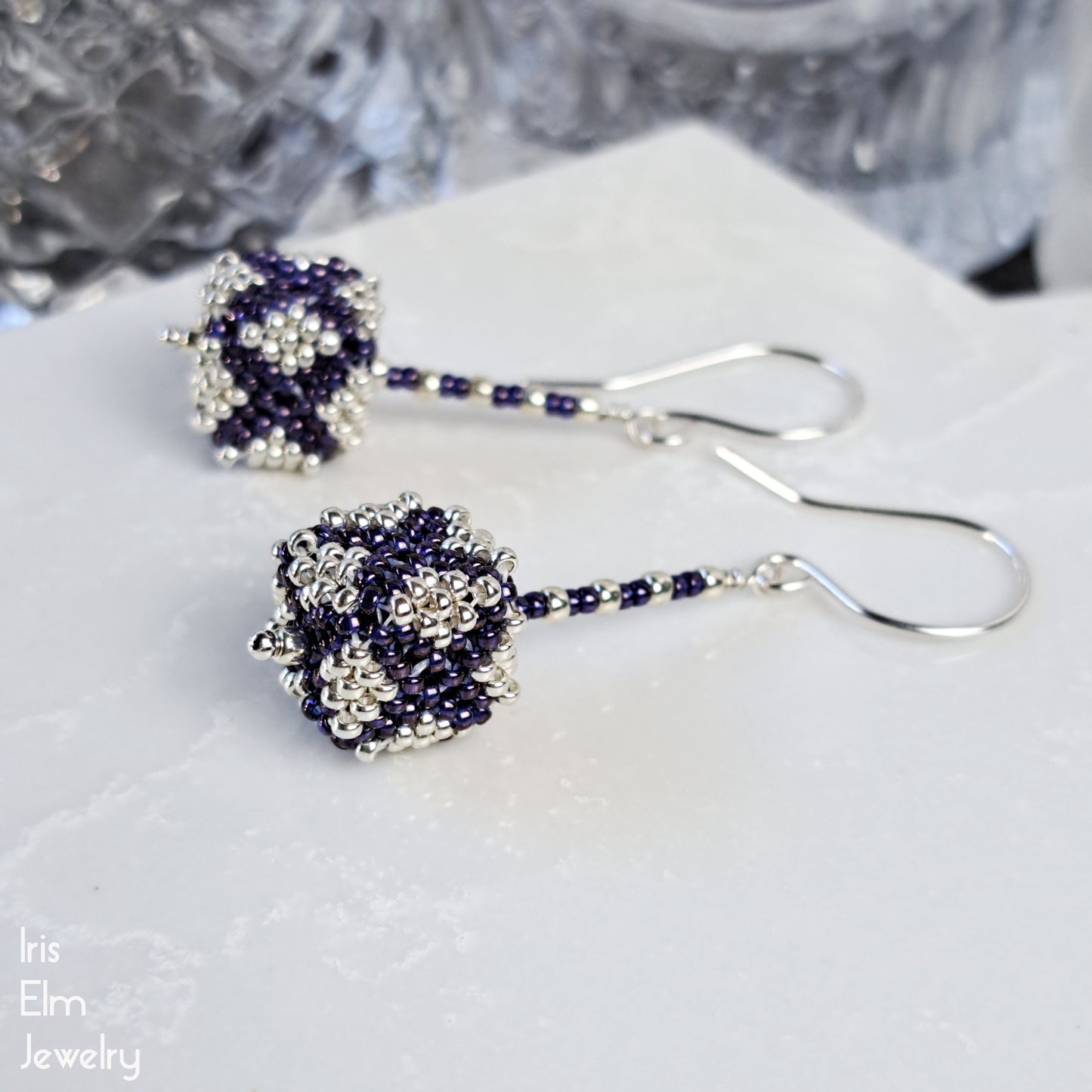 Pair of purple and silver seed bead cube shaped beaded earrings on a white surface with 'Iris Elm Jewelry' branding.