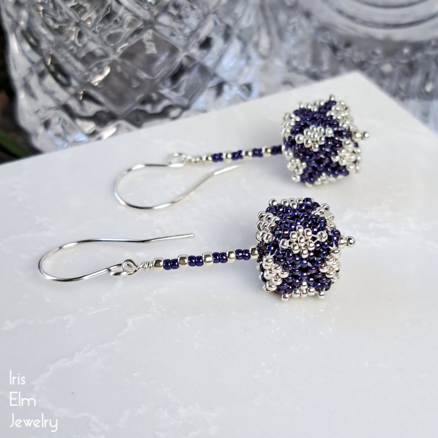 Pair of beaded purple and silver seed bead cube shaped earrings on a white surface with 'Iris Elm Jewelry' branding.