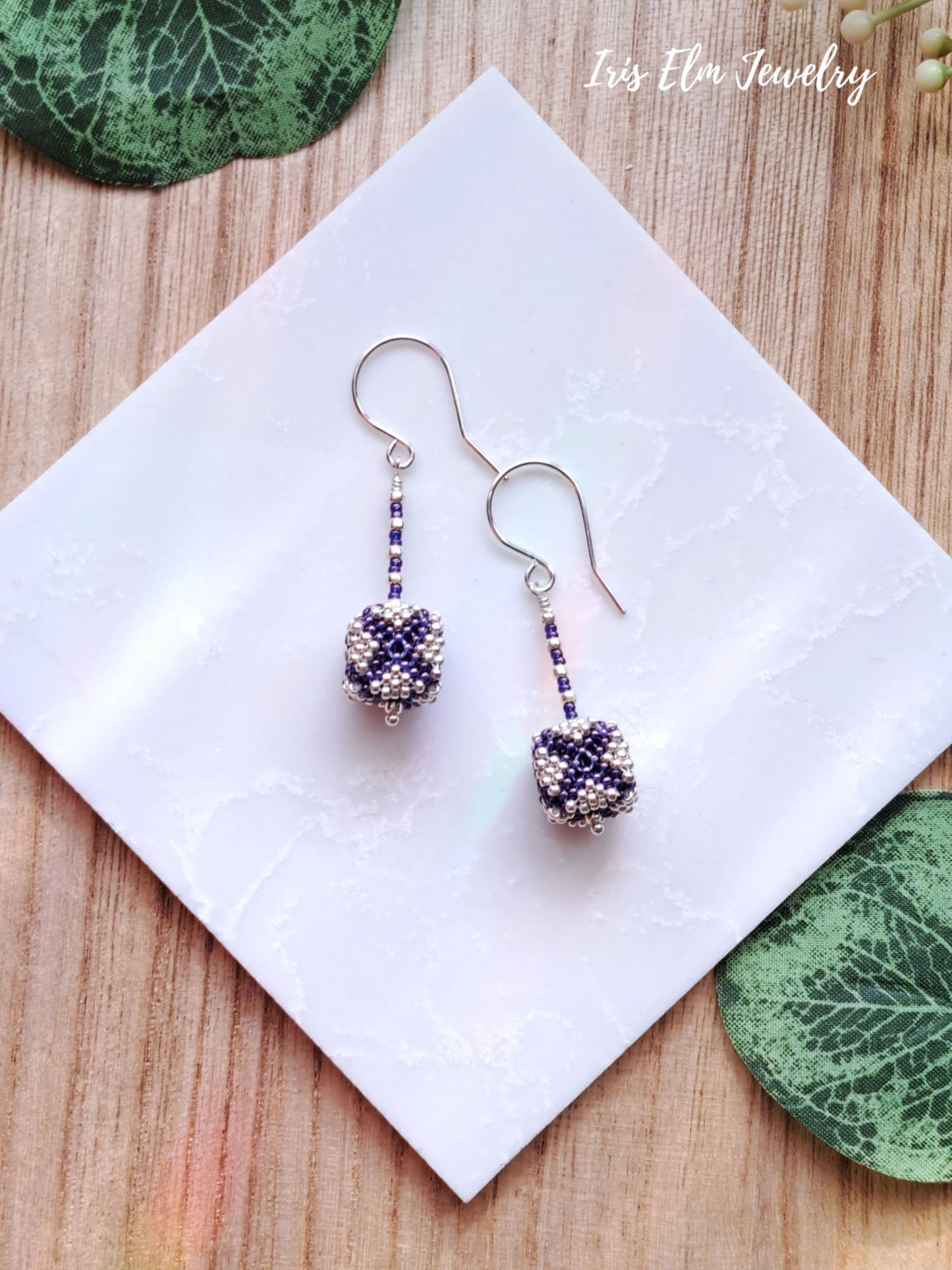 Pair of beaded purple and silver seed bead cube earrings on a white napkin with 'Iris Elm Jewelry' branding.