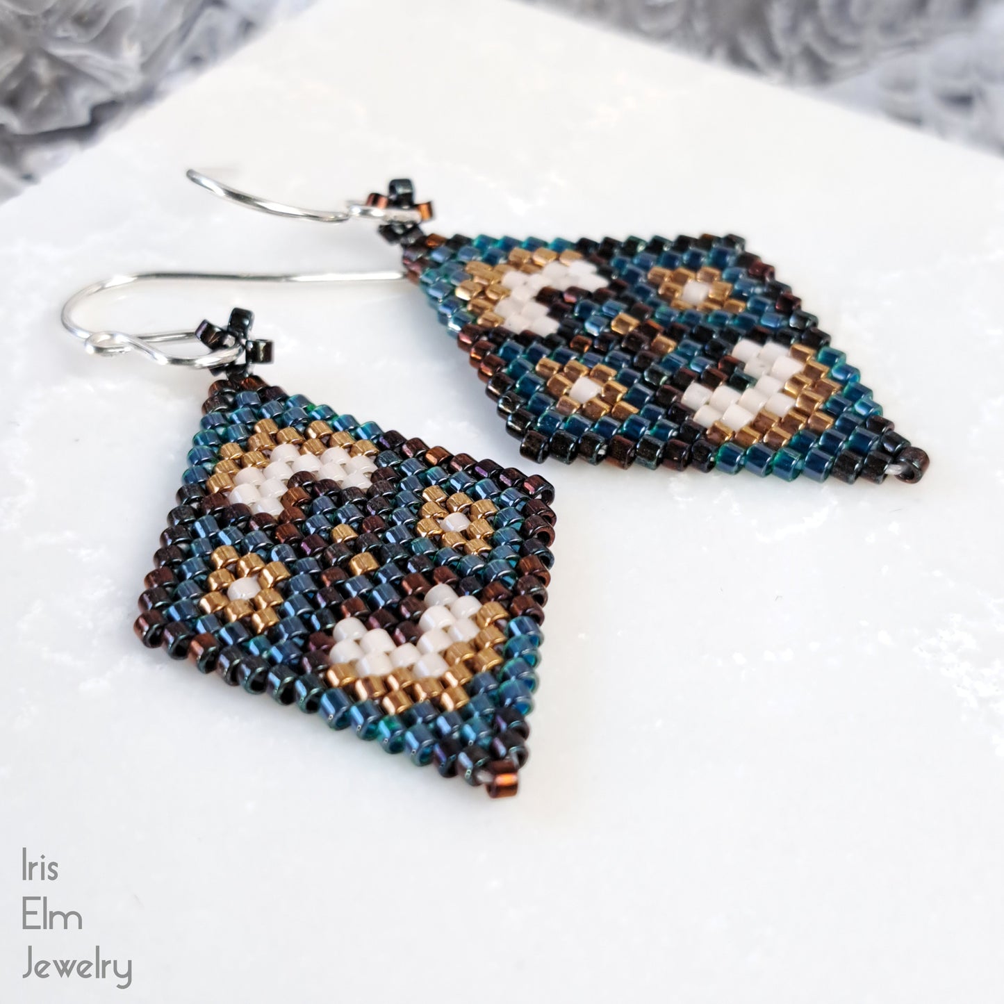 Pair of beaded seed bead green and brown earrings on a white surface with 'Iris Elm Jewelry' branding.