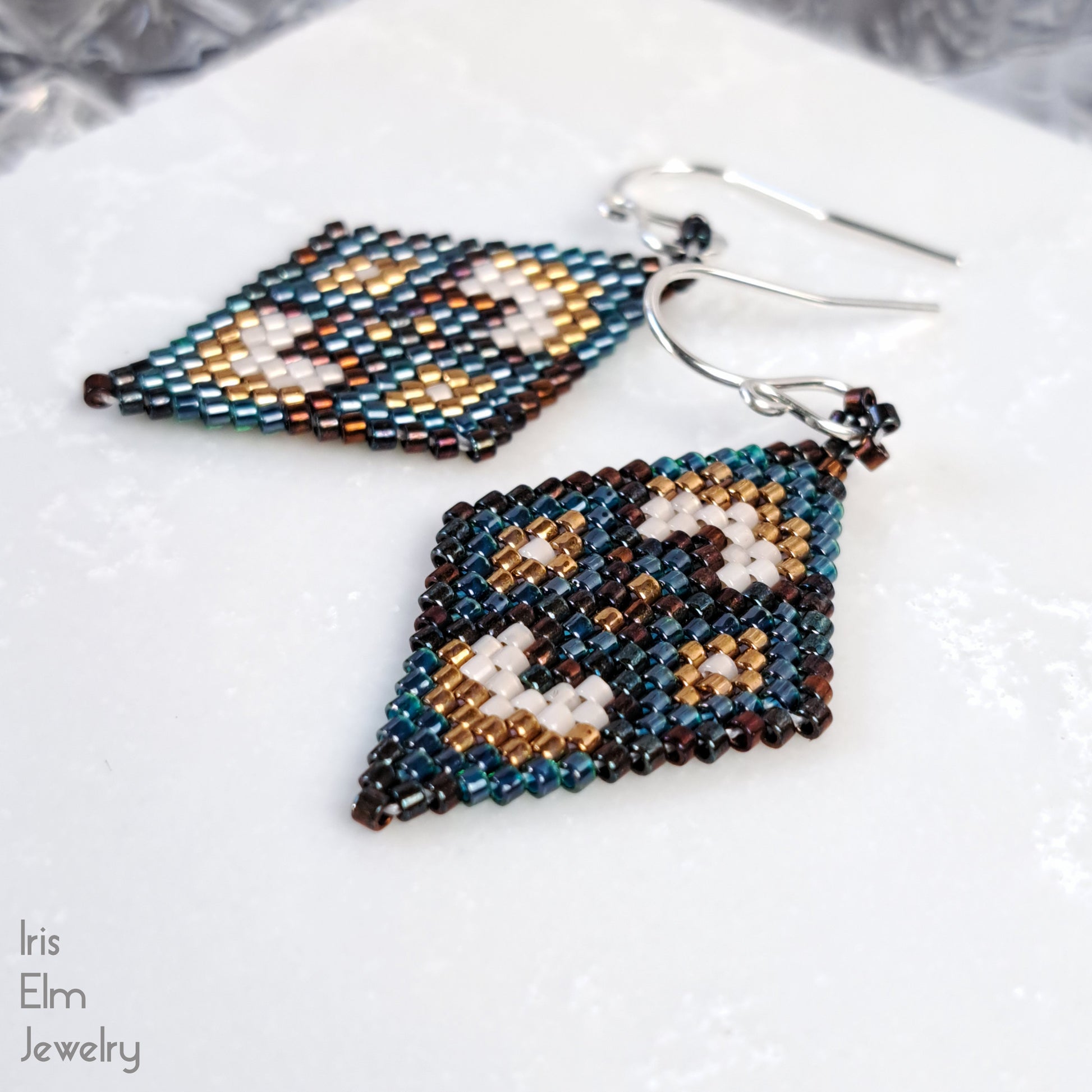 Beaded diamond-shaped handcrafted earrings with sterling silver ear wires on a white surface with 'Iris Elm Jewelry' branding.