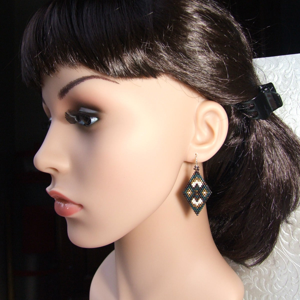 Mannequin head with dark hair styled in a ponytail, wearing beaded earrings.