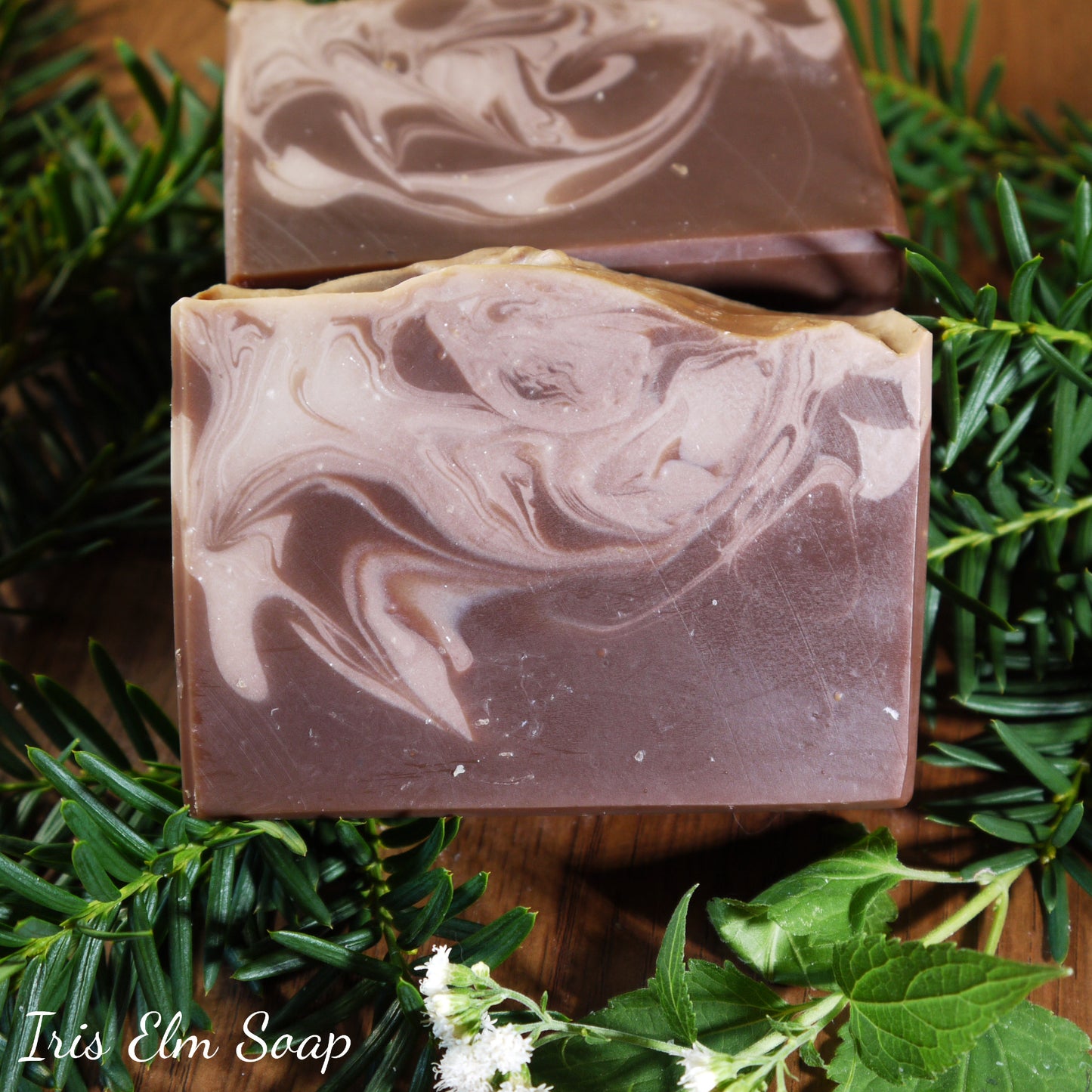 Two swirled vanilla soap bars on a wooden surface with greenery