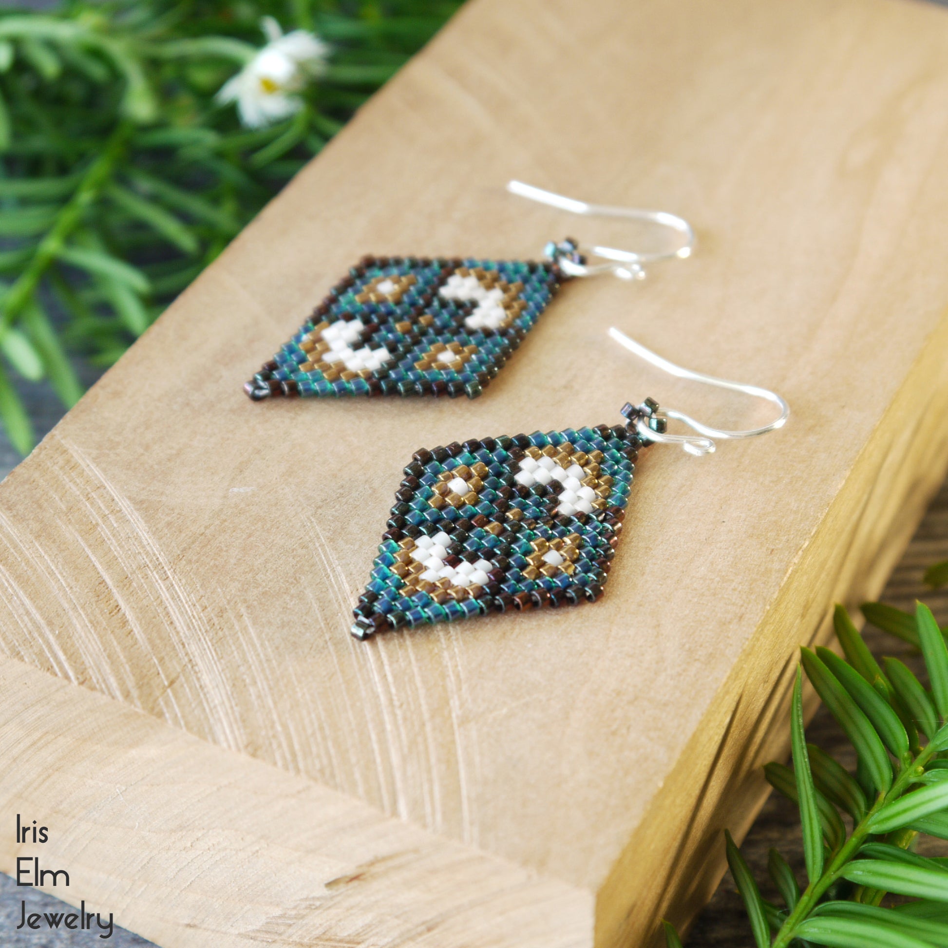Beadwoven diamond shape seed bead earrings on a wooden surface with greenery in the background