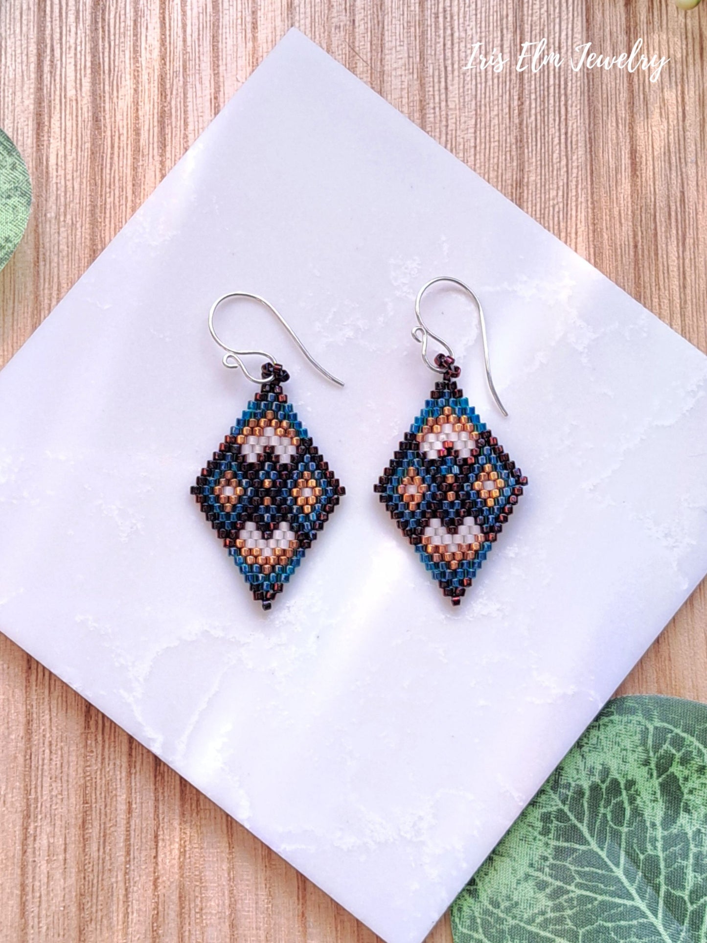 Beaded diamond shape brown and green seed bead earrings on a white square with 'Iris Elm Jewelry' branding.