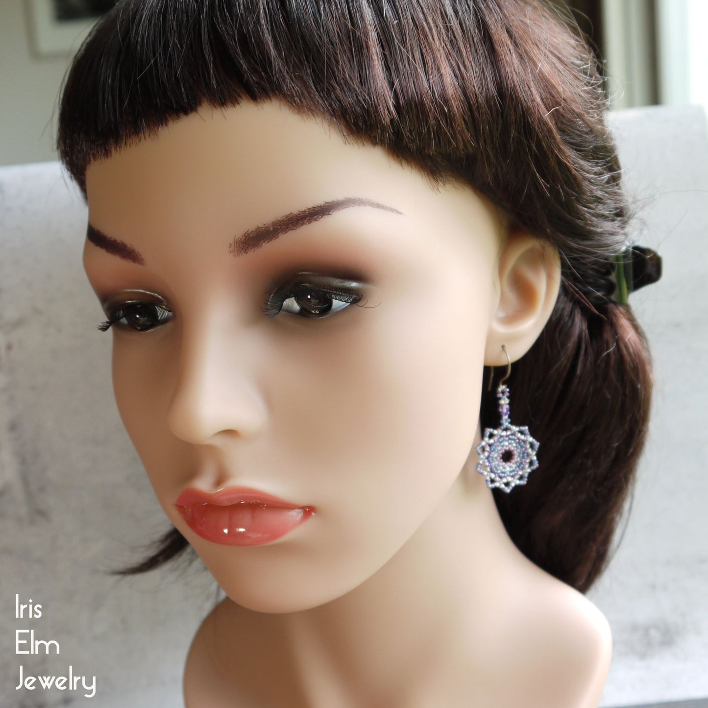 Mannequin head with dark hair and makeup wearing a purple earring, with 'Iris Elm Jewelry' branding.
