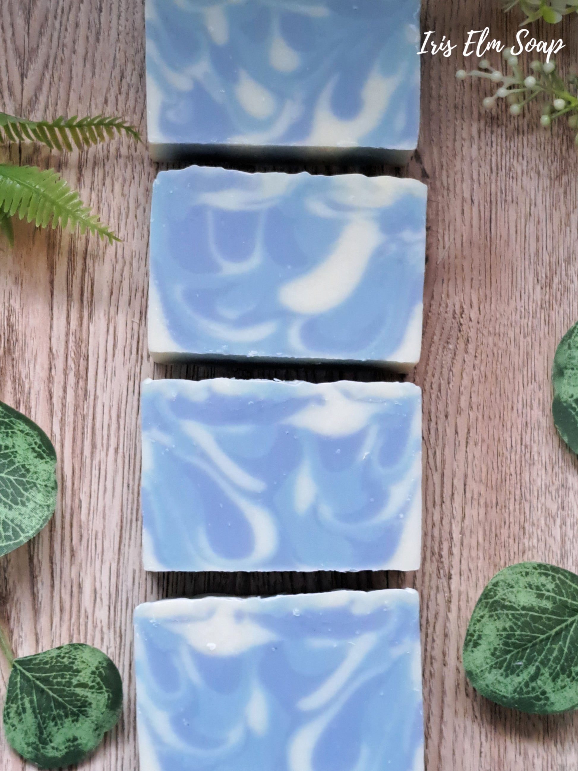 Blue and white swirled gentlemen handmade soap bars on a wooden surface with green leaves.