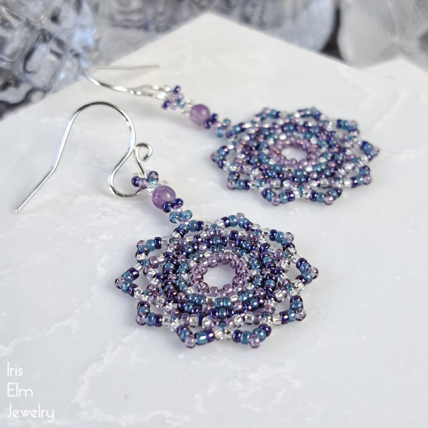 Beaded seed bead mandala purple earrings on a white fabric background with 'Iris Elm Jewelry' branding.