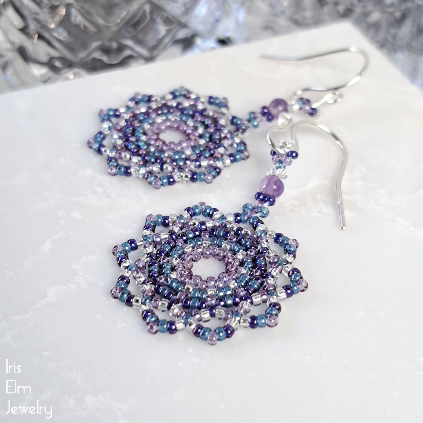 Beaded seed bead purple and blue mandala amethyst earrings on a textured white surface with 'Iris Elm Jewelry' branding.