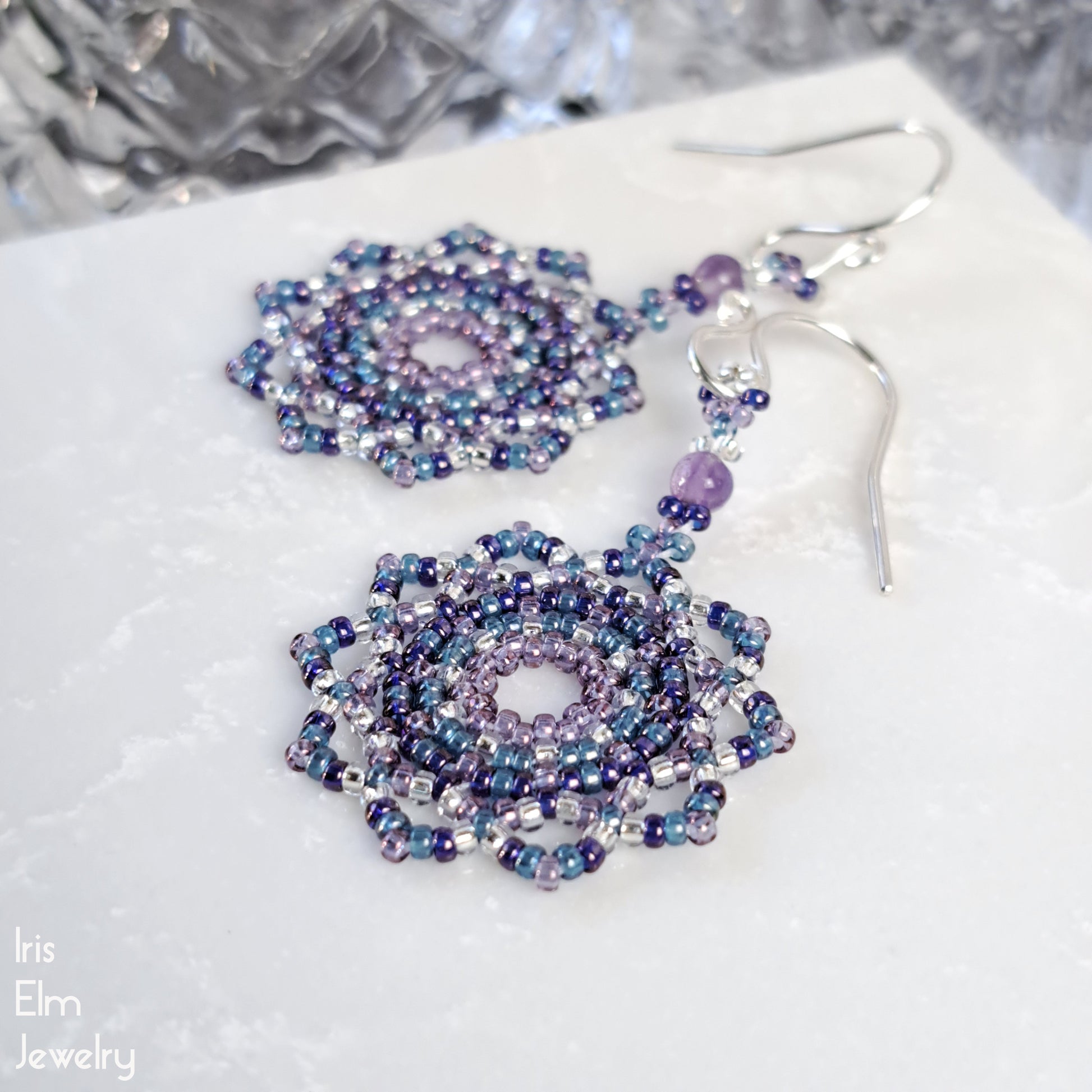 Beaded seed bead purple and blue mandala amethyst earrings on a textured white surface with 'Iris Elm Jewelry' branding.