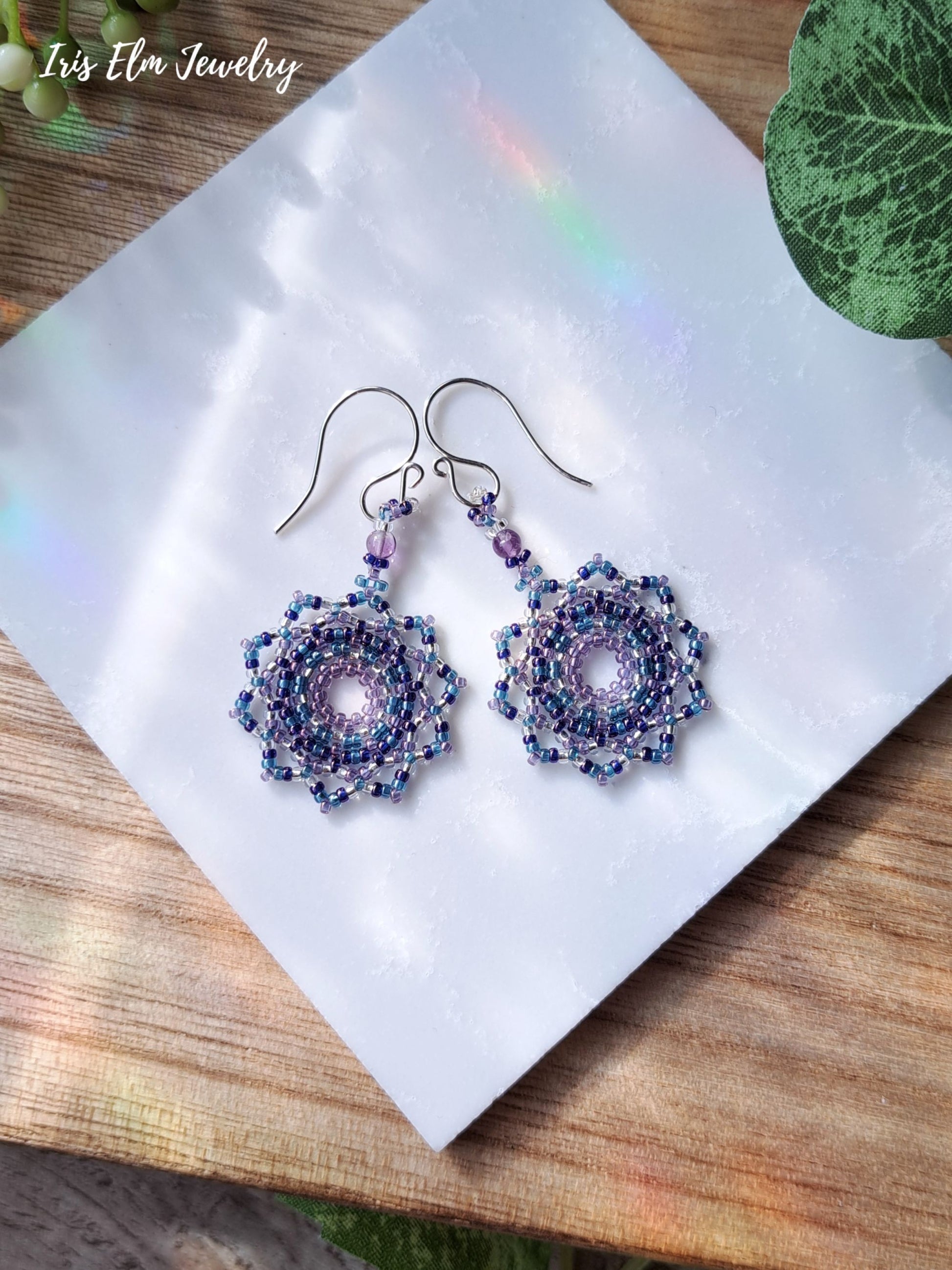 Pair of beaded seed bead amethyst mandala earrings on a white paper with 'Iris Elm Jewelry' branding.