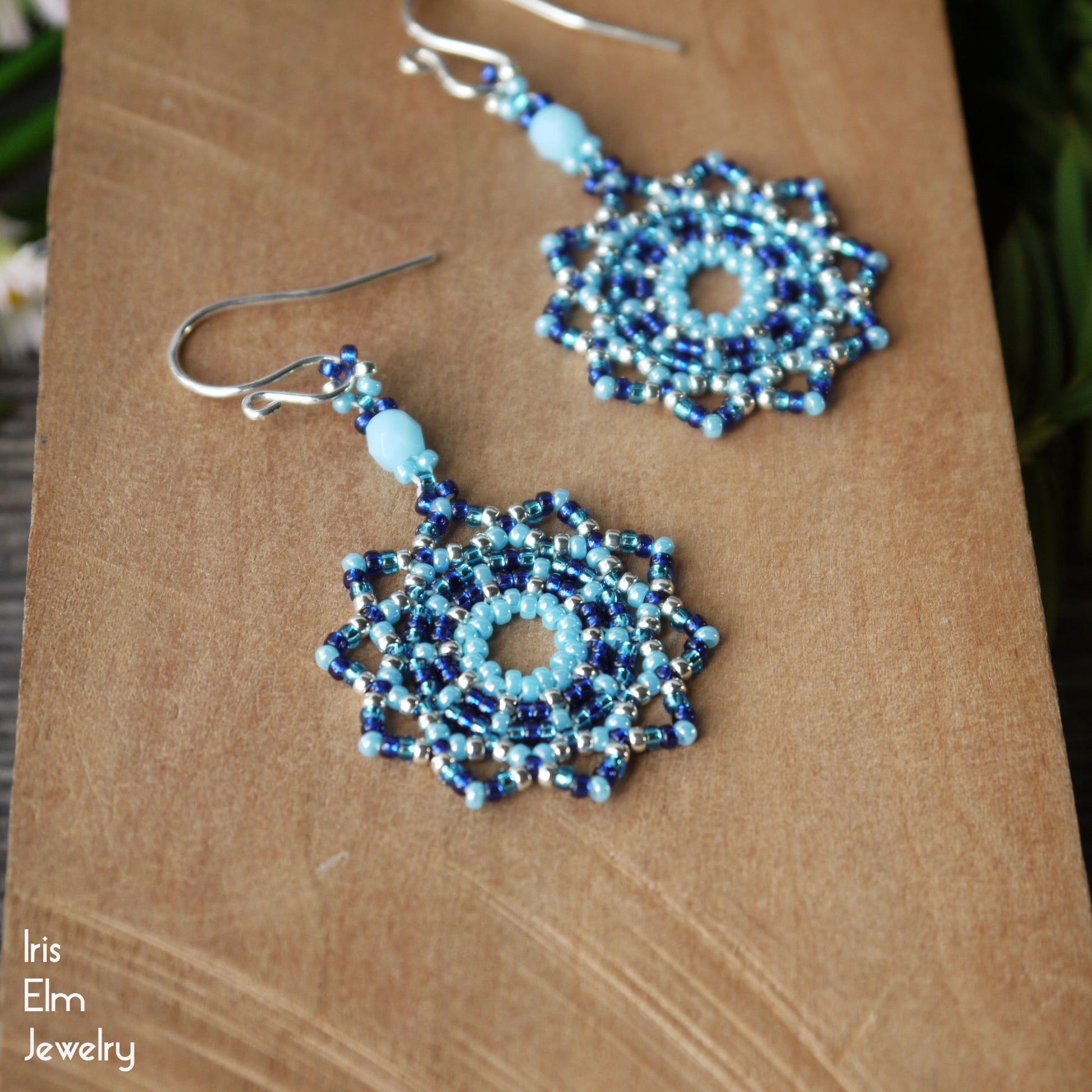 Blue beaded handmade circular beadwork earrings on a brown surface with 'Iris Elm Jewelry' branding.
