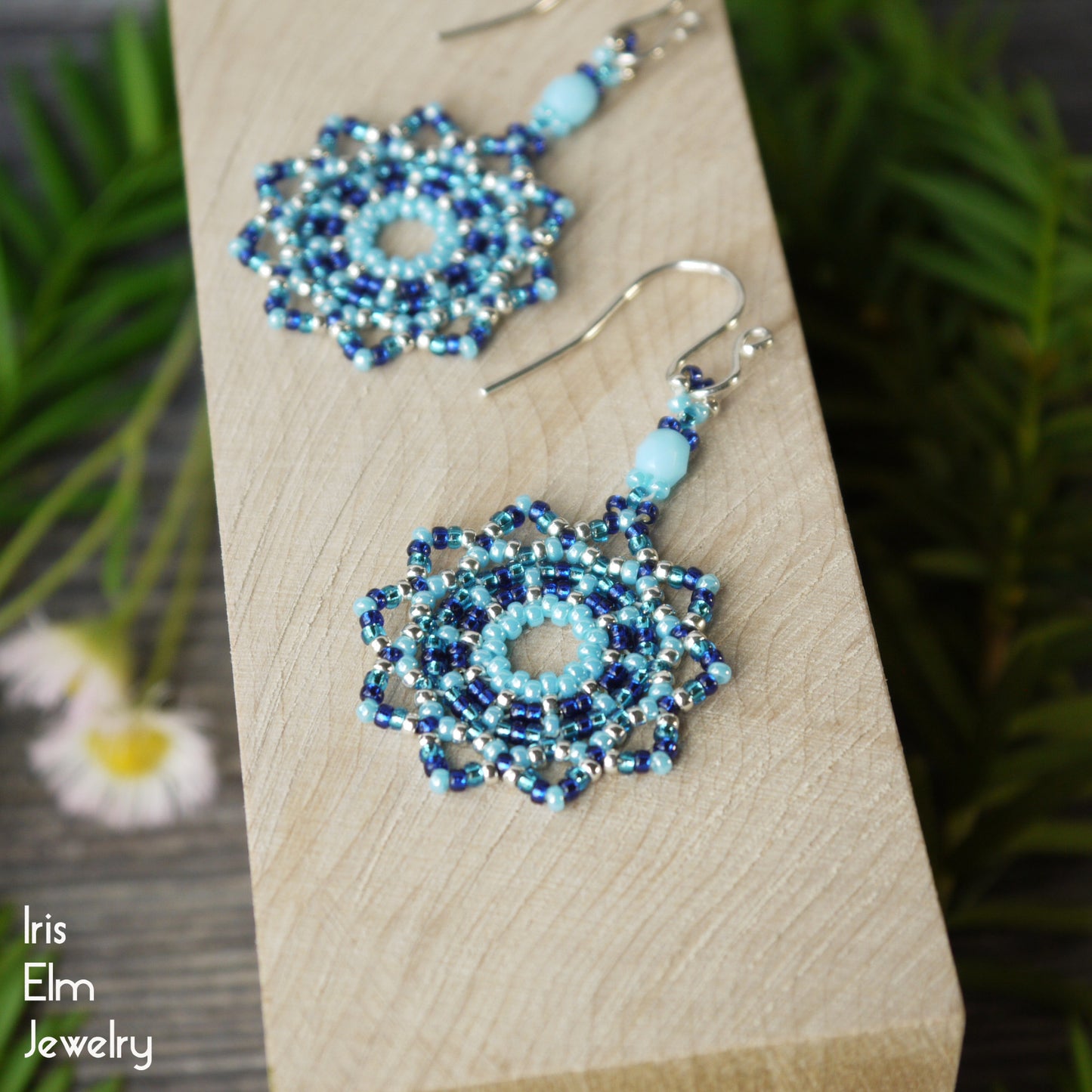 Pair of beaded blue dangle earrings on a wooden block with 'Iris Elm Jewelry' branding.