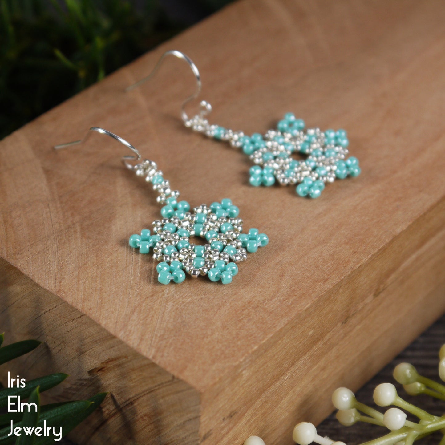 Turquoise beaded seed bead snowflake earrings on a wooden surface with 'Iris Elm Jewelry' branding.