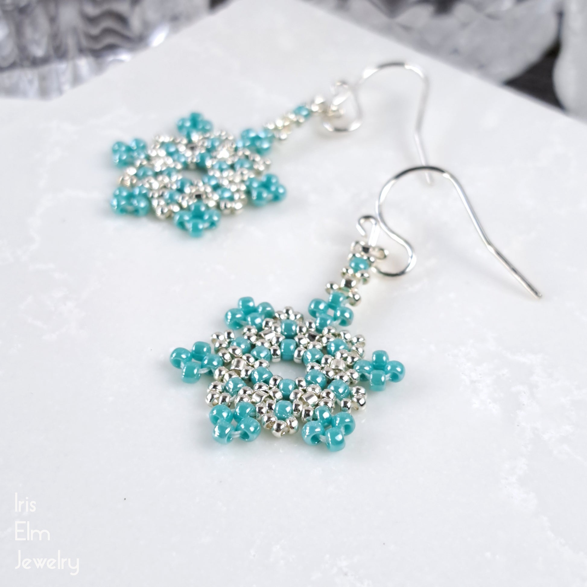 Turquoise and silver beaded snowflake seed bead earrings on a white surface