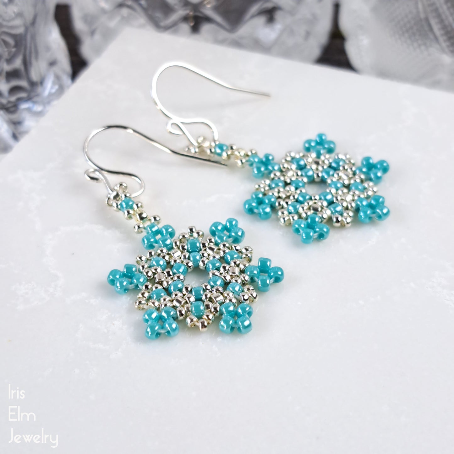 Pair of beaded winter snowflake earrings with turquoise beads on a white surface