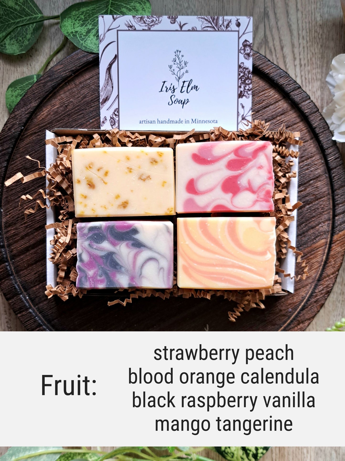 Box of assorted fruit scented mini handmade soaps with a 'Iris Elm Soap' card on a wooden surface.