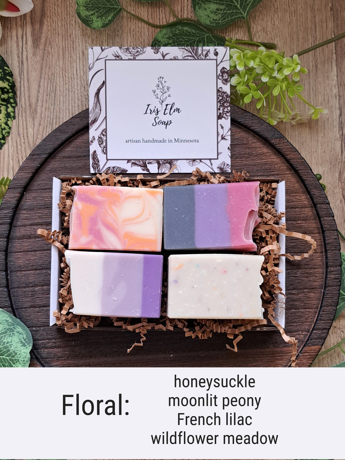 Set of four floral scented soap bars in a box with a label on a wooden surface.