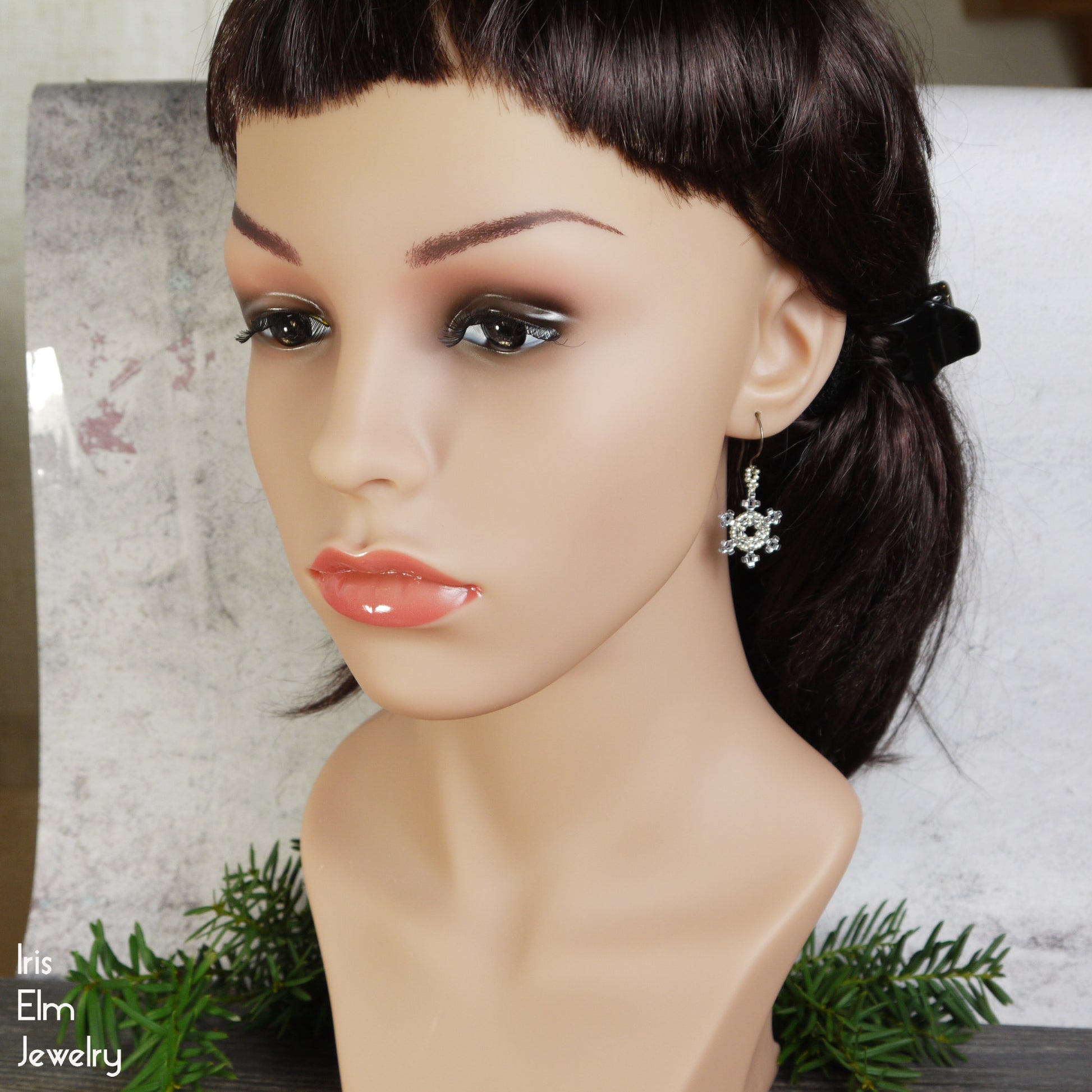 Mannequin head with a ponytail wearing a silver and blue snowflake earring, with 'Iris Elm Jewelry' branding.