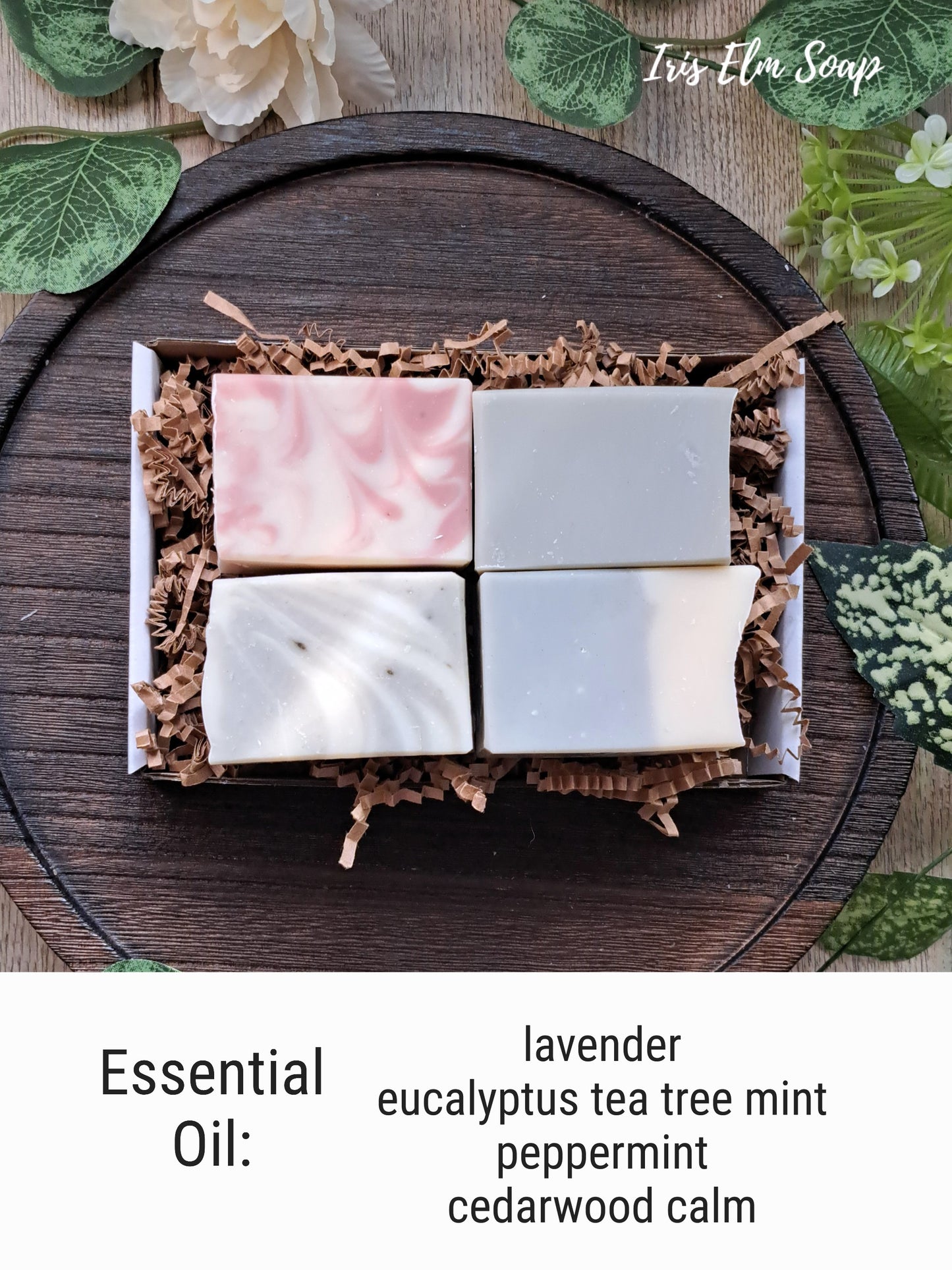 Four essential oil handmade soap bars in a gift box with decorative elements on a wooden surface.