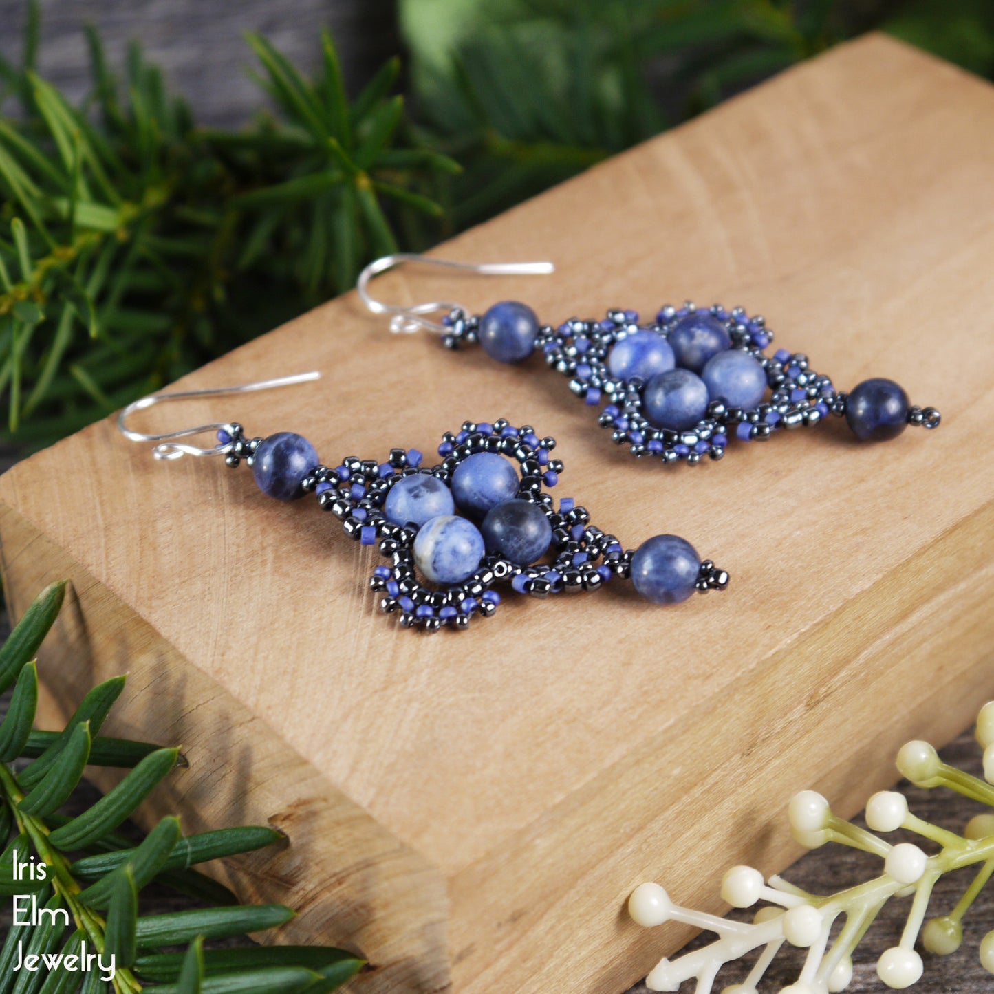 Blue beaded sodalite stone earrings on a wooden block with greenery in the background