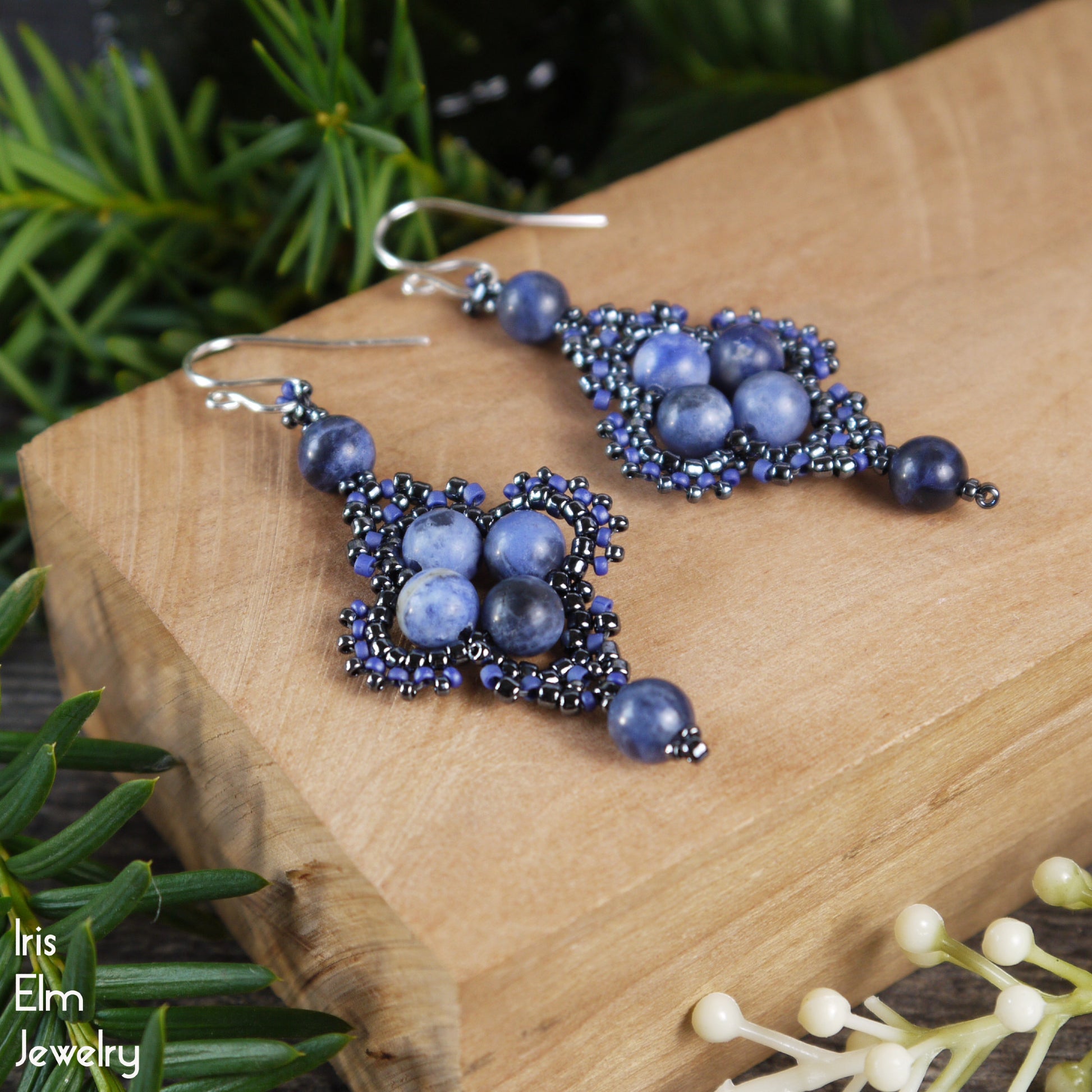 Blue beaded gemstone sodalite earrings with sterling silver ear wires on a wooden block with greenery in the background