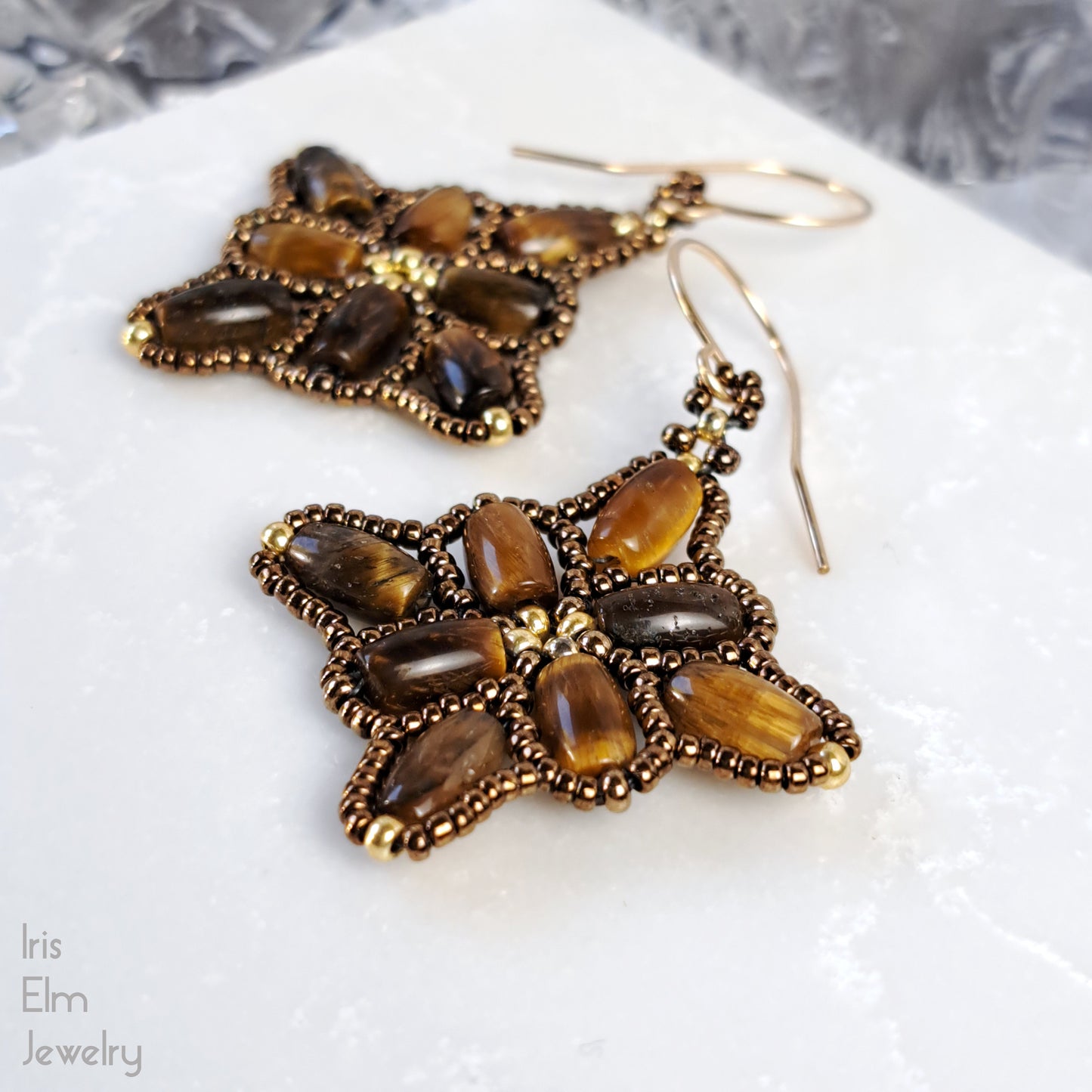 Pair of handmade quilt shape earrings with brown tiger eye stones on a white surface