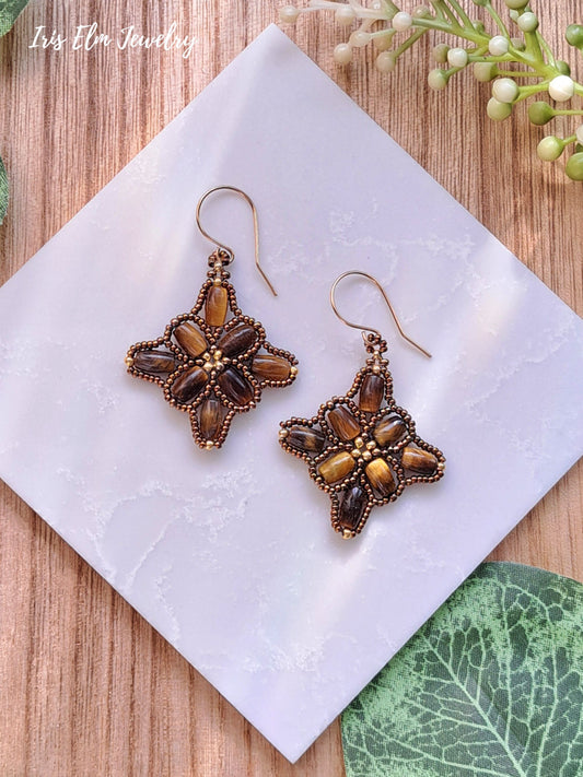 Decorative brown tiger eye beadwork earrings on a white marble stone with a natural wood background