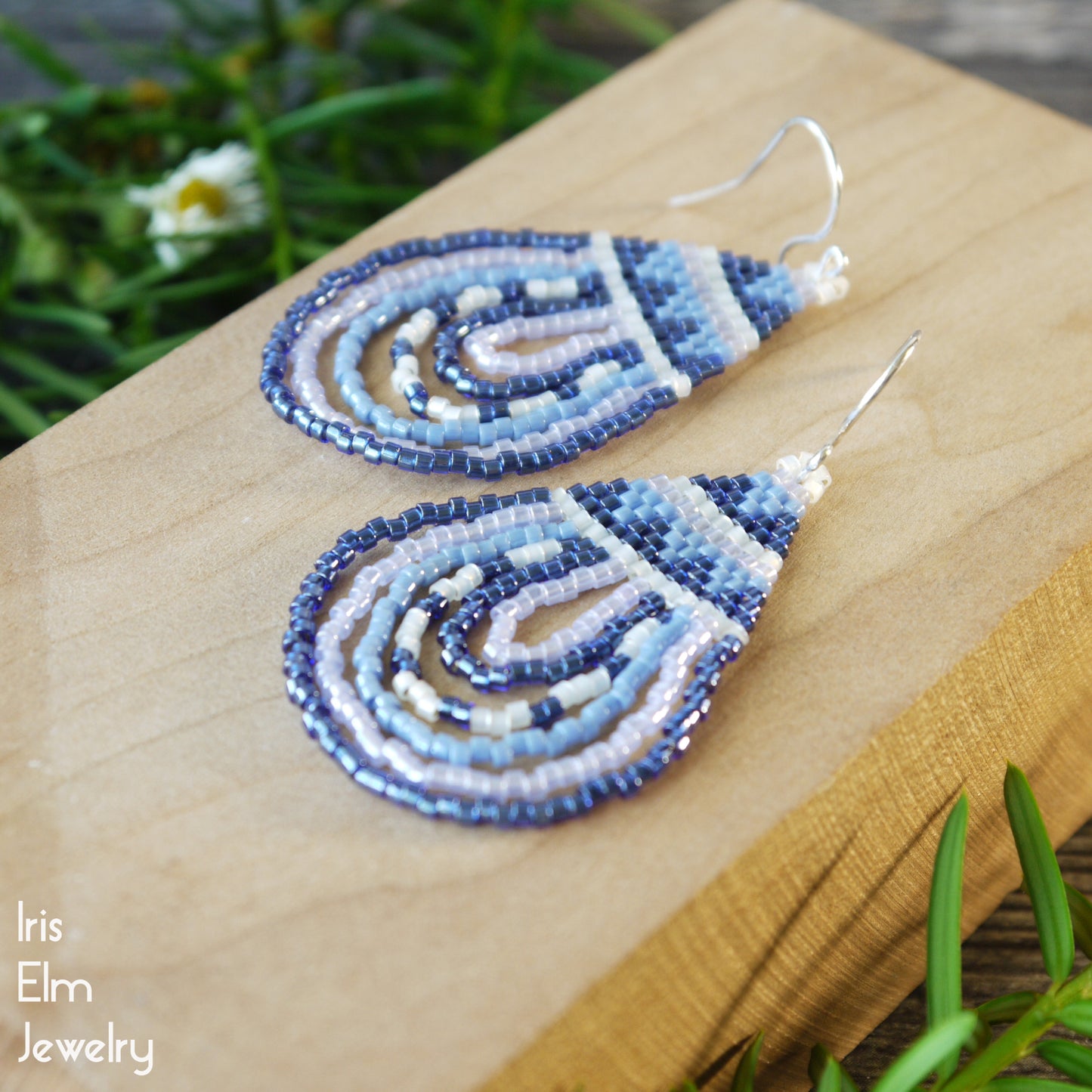 Blue and white beaded teardrop seed bead handmade earrings on a wooden surface with 'Iris Elm Jewelry' branding.
