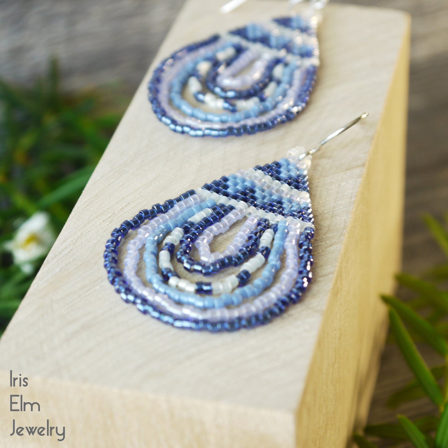 Beaded ocean blue teardrop glass earrings on a wooden block with a natural background