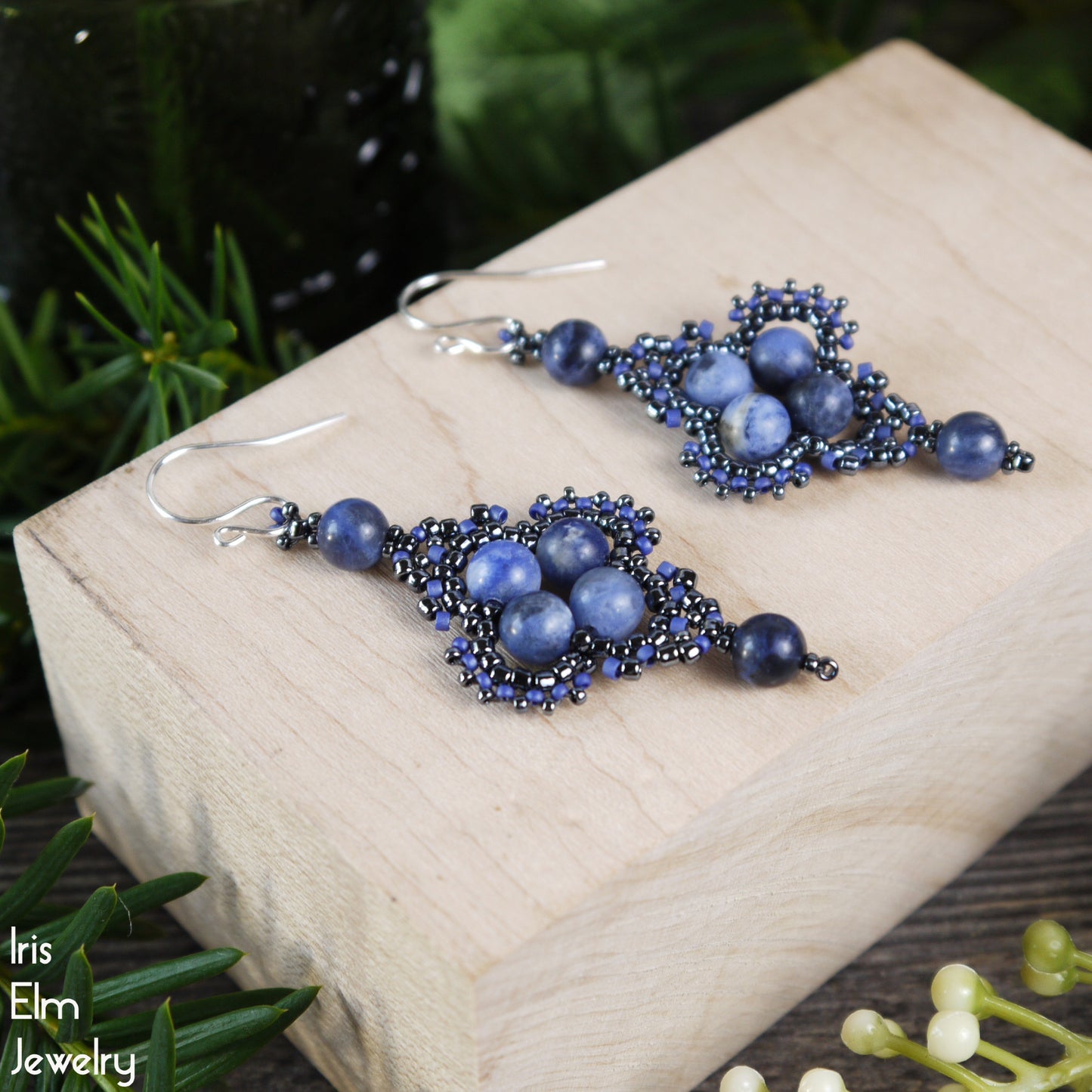 Blue sodalite and seed bead beadwork earrings on a wooden block with greenery in the background