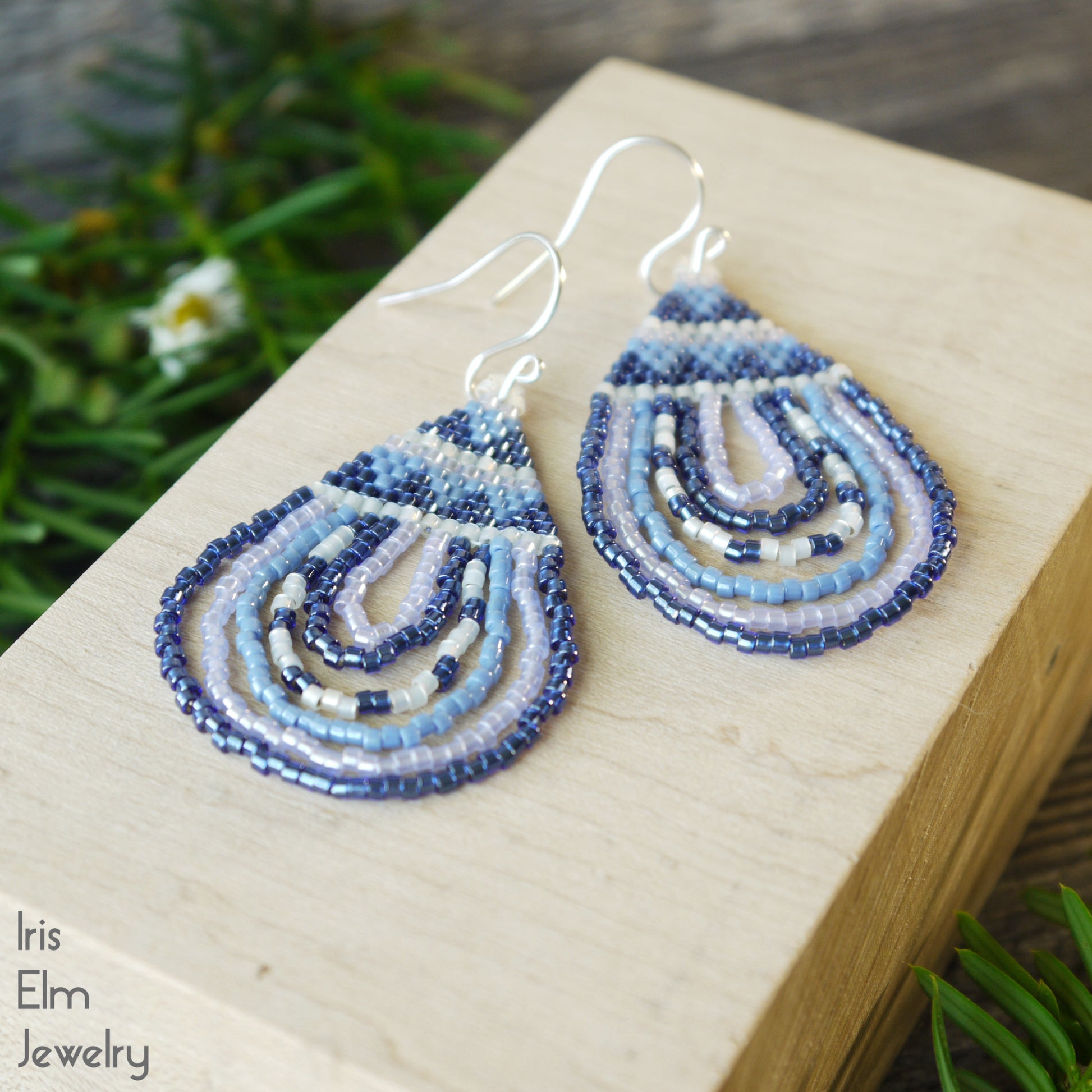 Handmade Blue and white beaded teardrop shaped earrings on a wooden block with a natural background