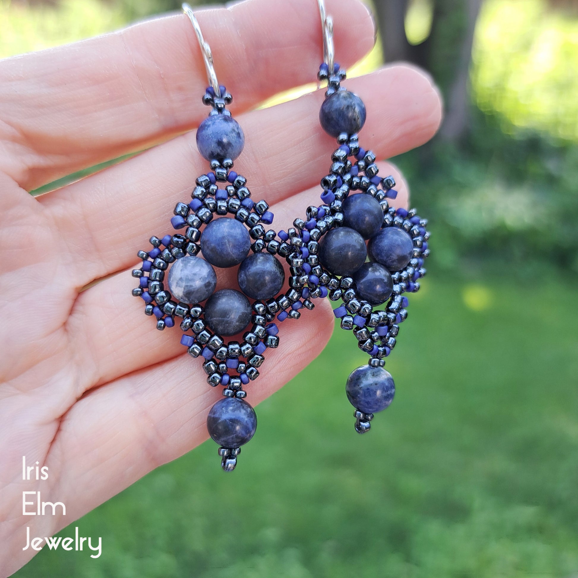 Blue beaded earrings held in a hand with a blurred green background