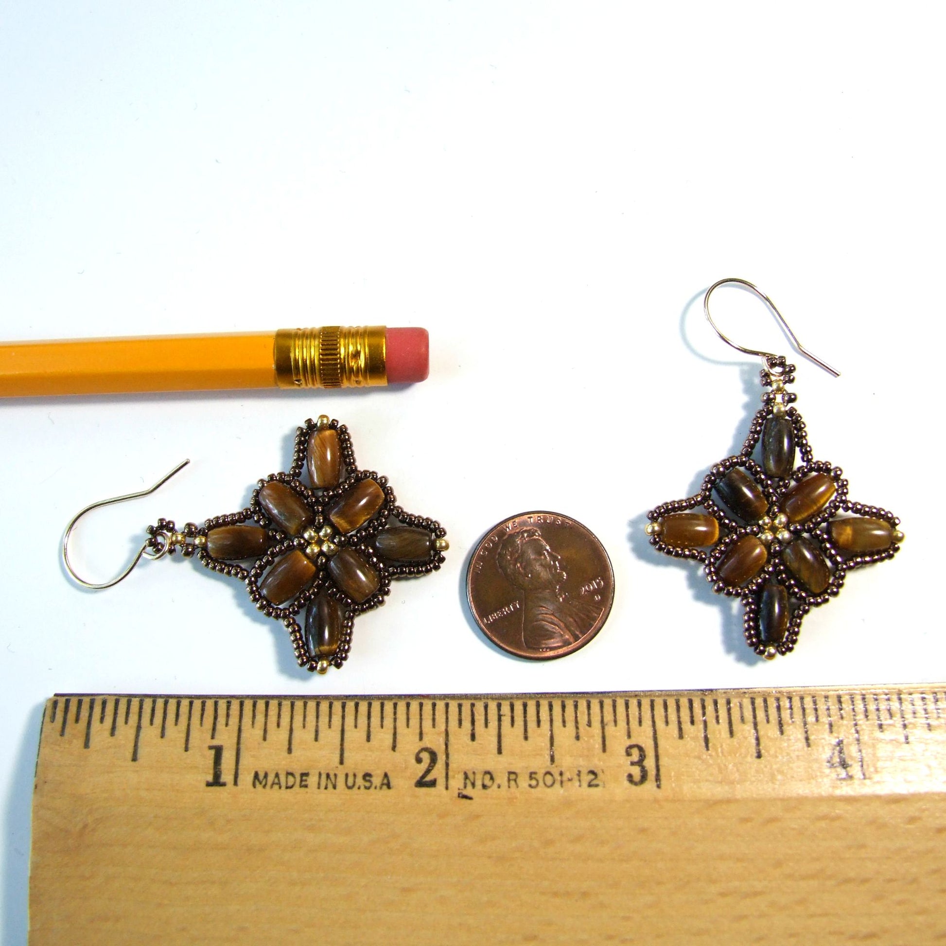 2 inches long Pair of decorative tiger eye beadwork earrings next to a pencil and penny on a white background with a ruler for scale.