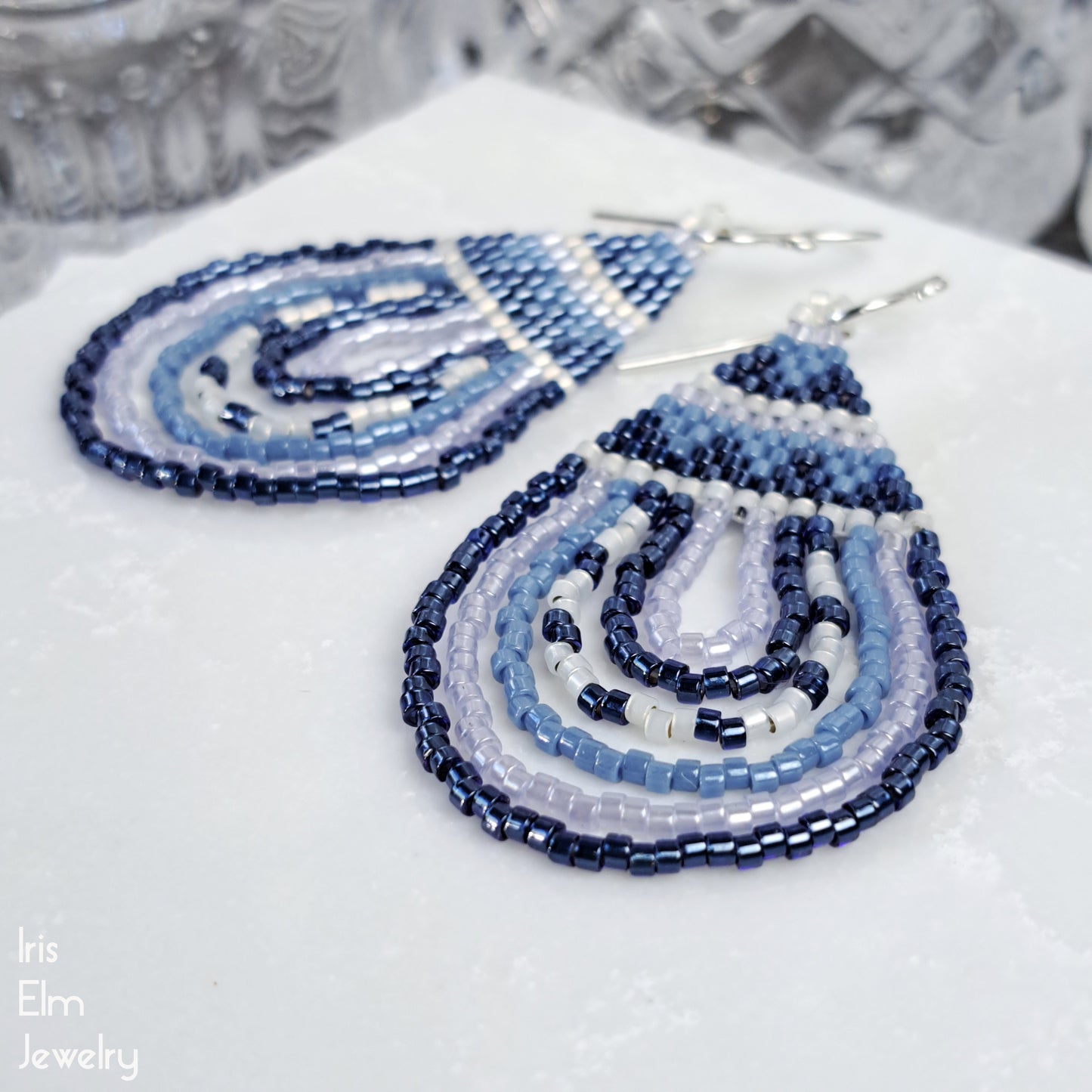 Beaded seed bead teardrop earrings with blue and white pattern on a textured surface