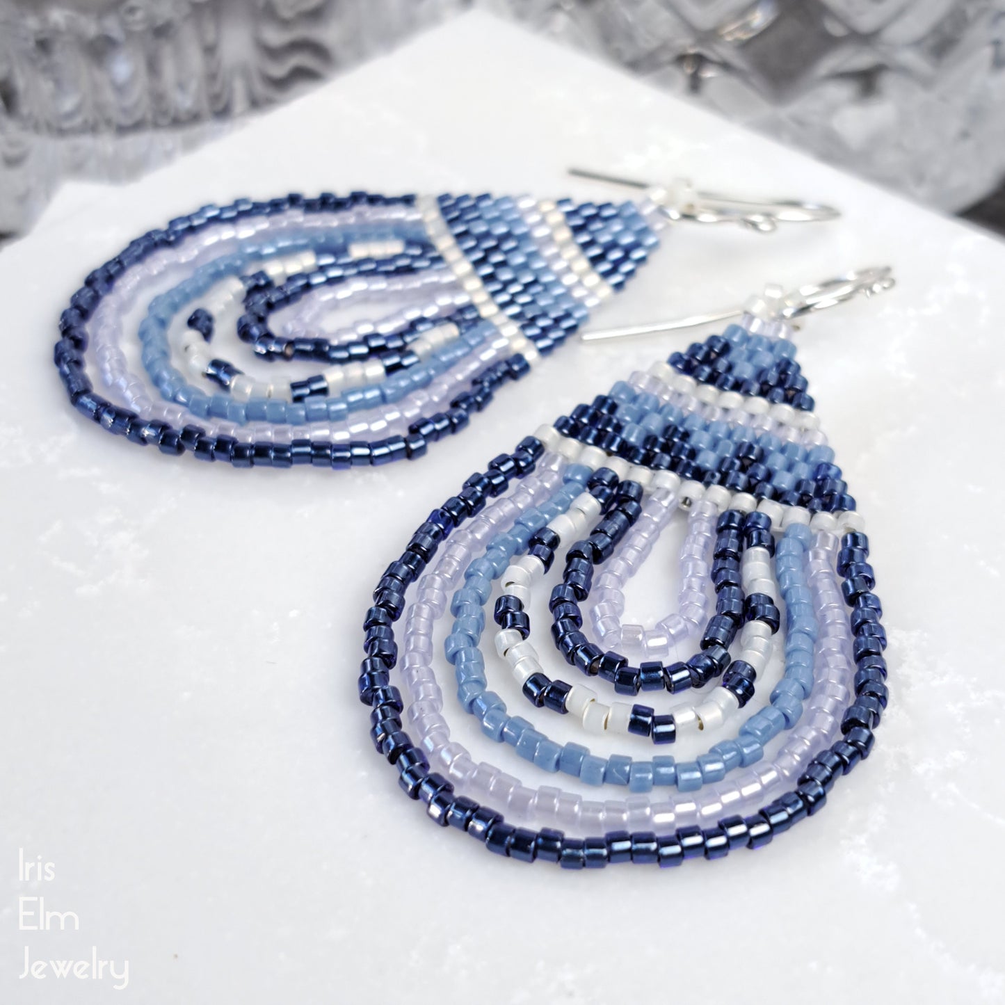 Blue beaded teardrop seed bead sterling silver earrings on a white surface with a blurred background