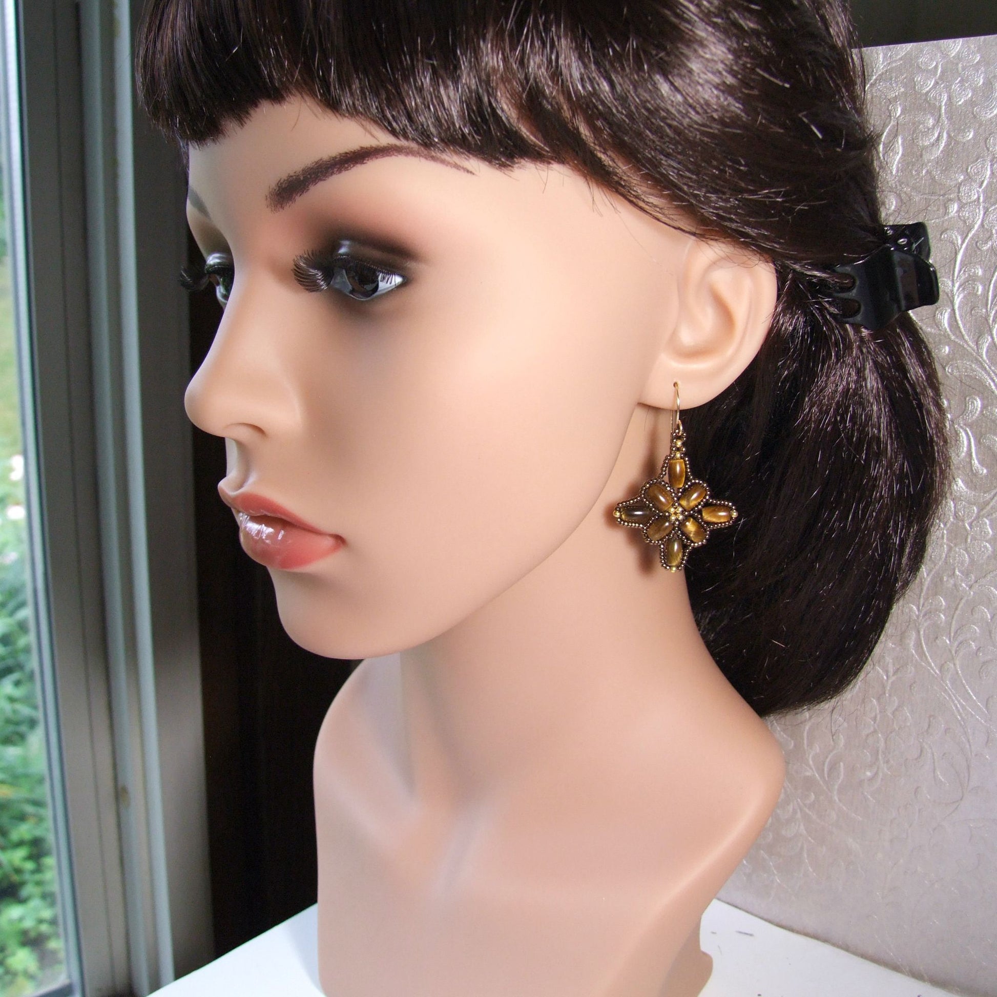 Mannequin head with a tiger eye quilt earring on a neutral background