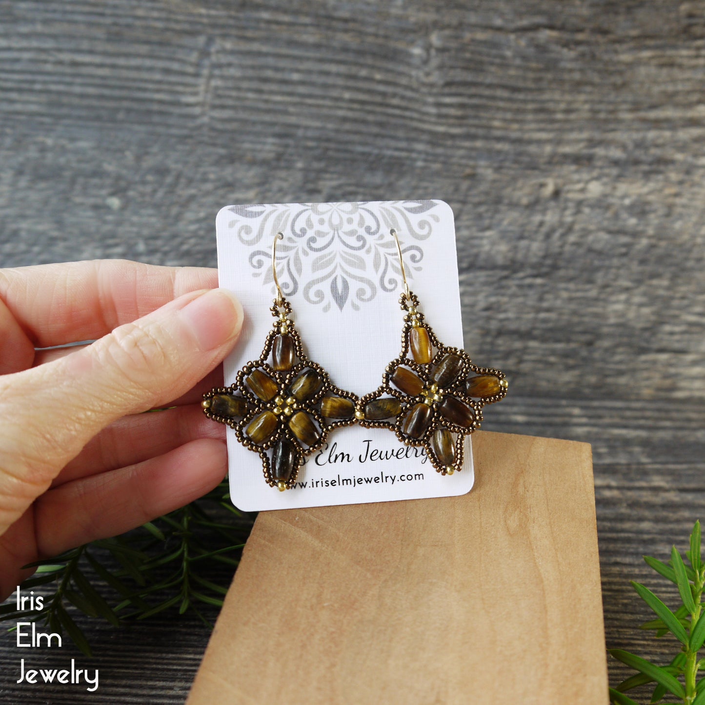 Pair beaded brown tiger eye earrings on a 'Iris Elm Jewelry' card against a wooden background