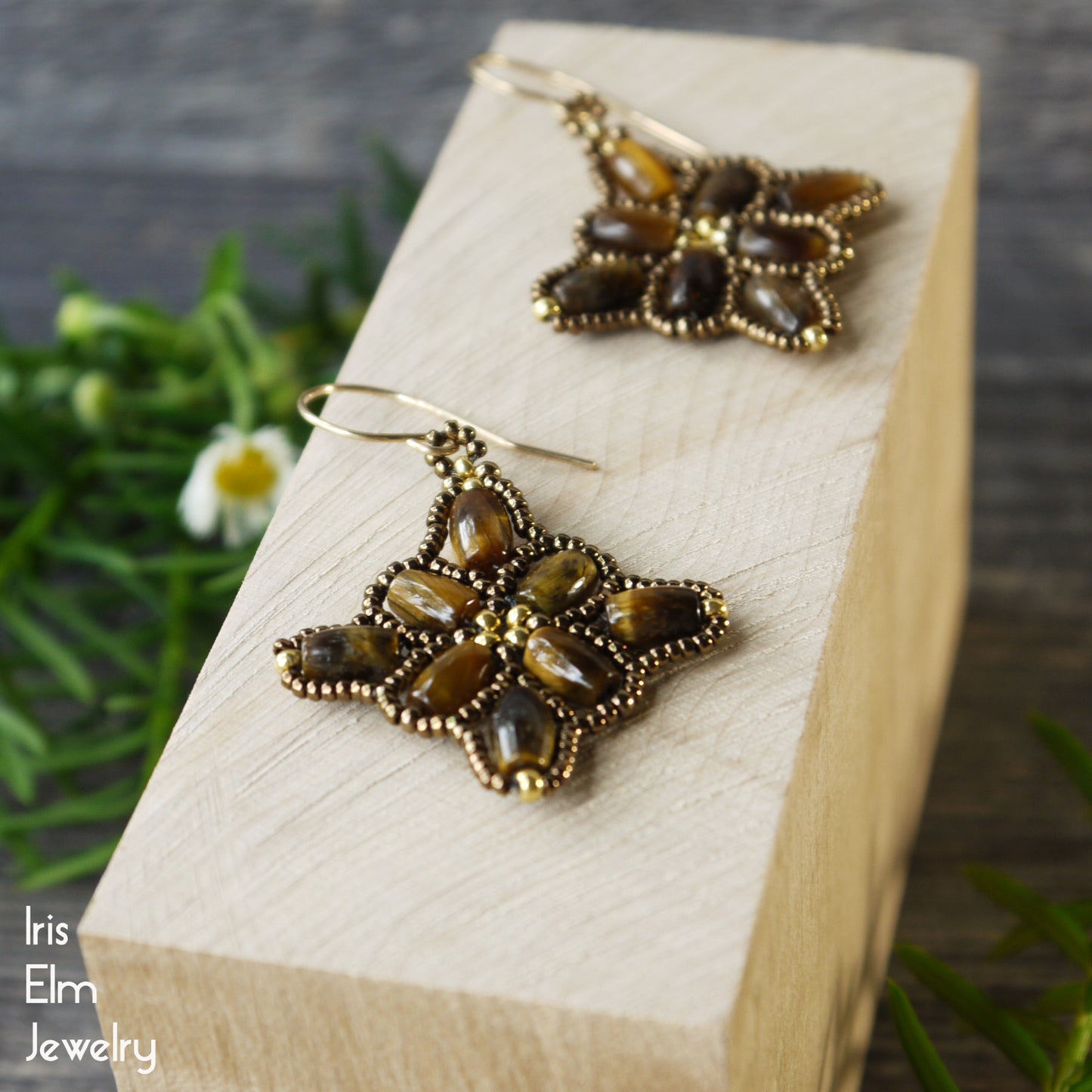 beadwork earrings with brown tiger eye stones encircled by tiny glass seed beads on a wooden block, brand 'Iris Elm Jewelry' visible.