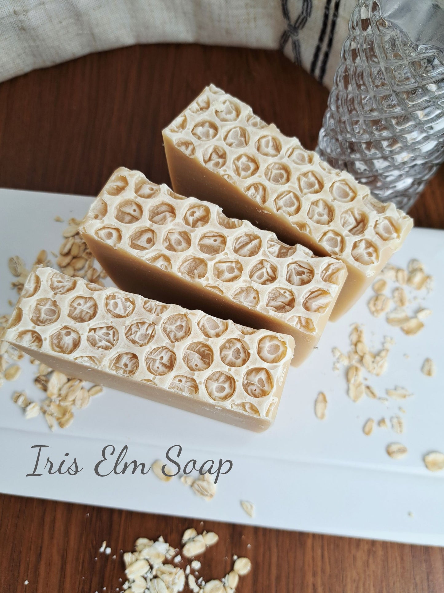 Three bars of oatmeal honey handmade soap with a honeycomb pattern on a white surface, labeled 'Iris Elm Soap'.
