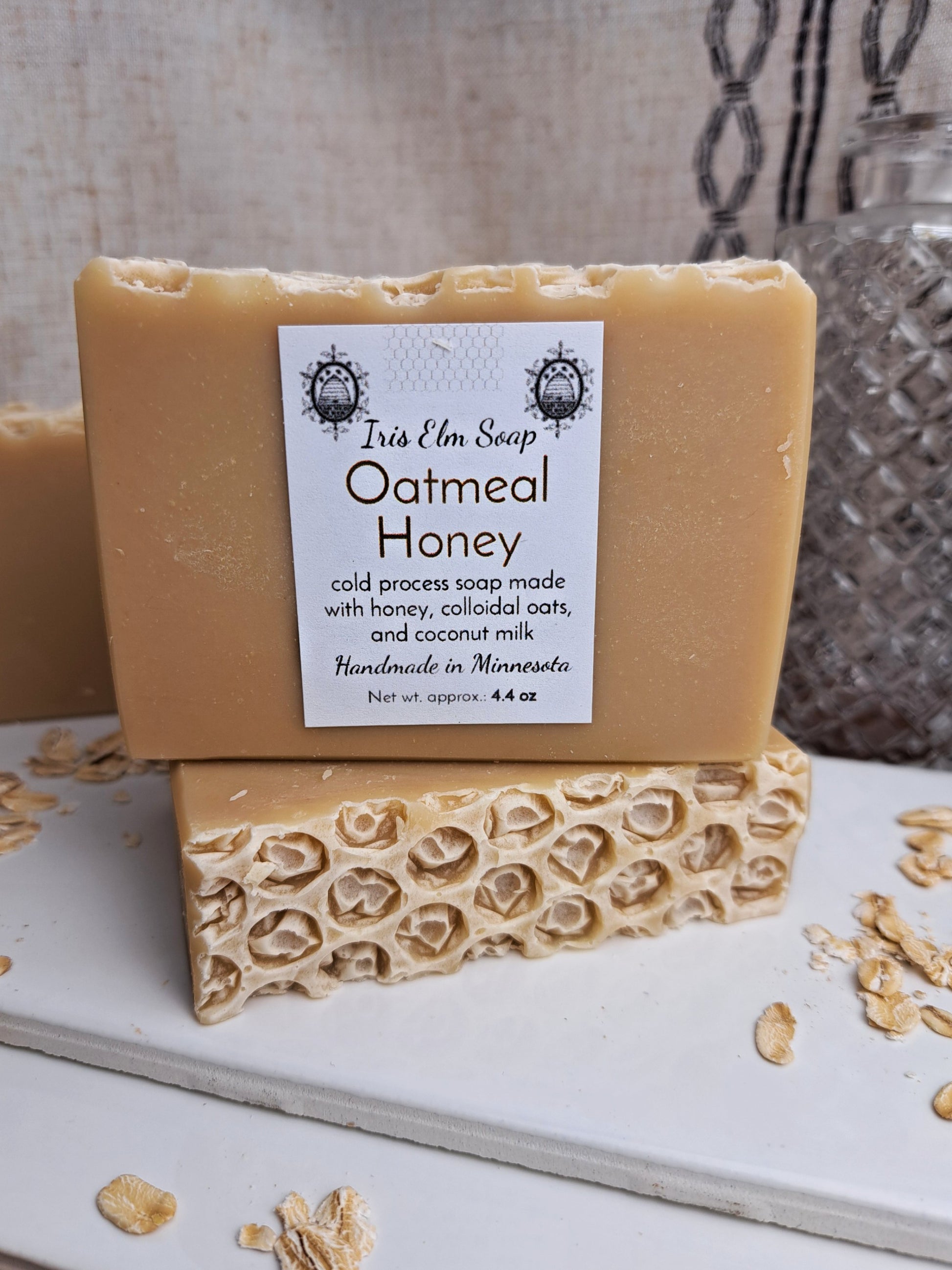 Two bars of oatmeal honey cold process soap with a visible label on a textured surface.